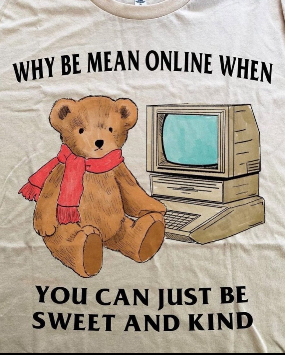 A t-shirt with a scarf wearing cartoon bear sat in front of an old desktop computer that says “why be mean online when you can just be sweet and kind”