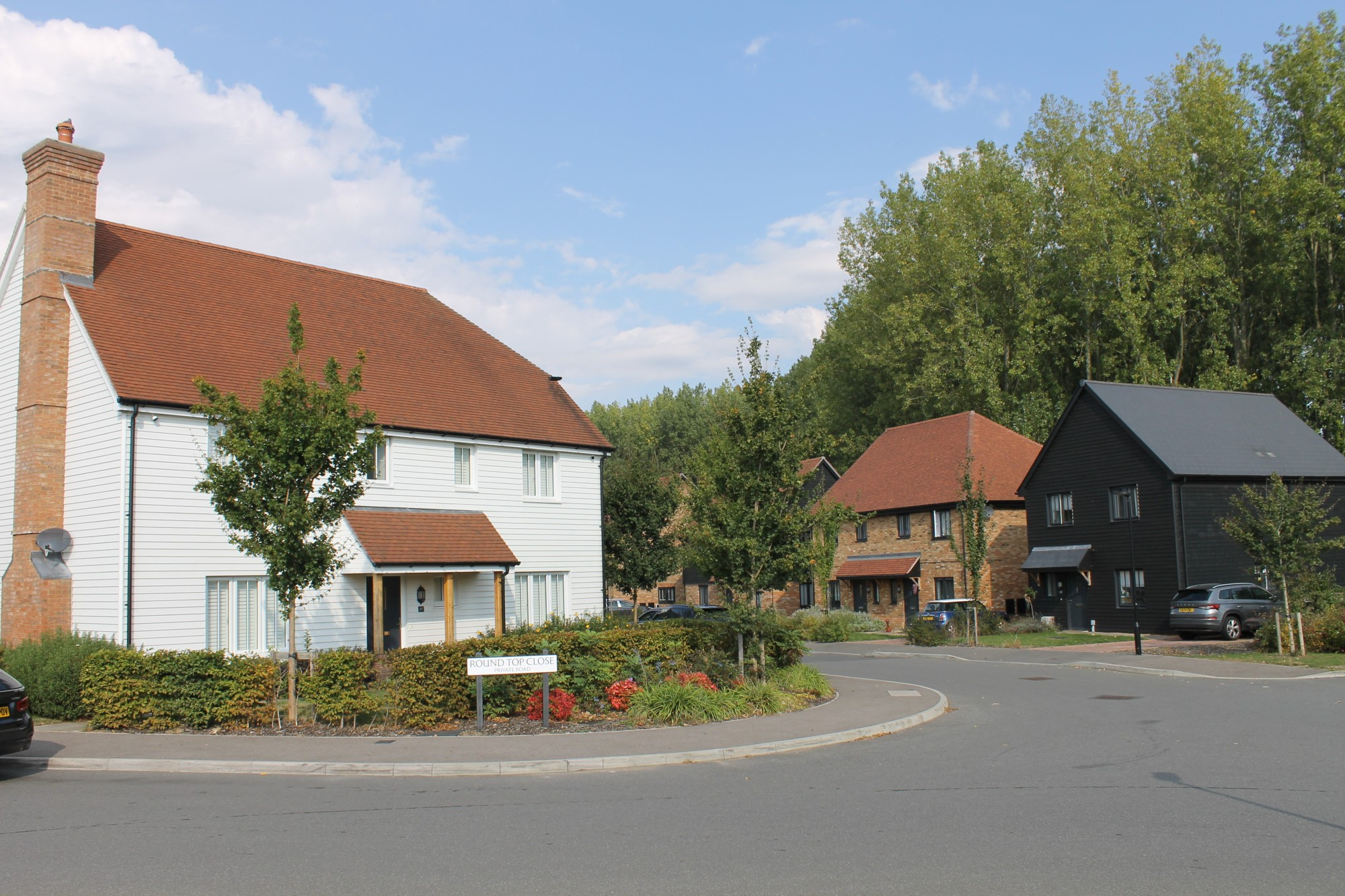 new rural housing - white weatherboarded and chimneyed house on corner with gabled black weatherboarded house and brick semi