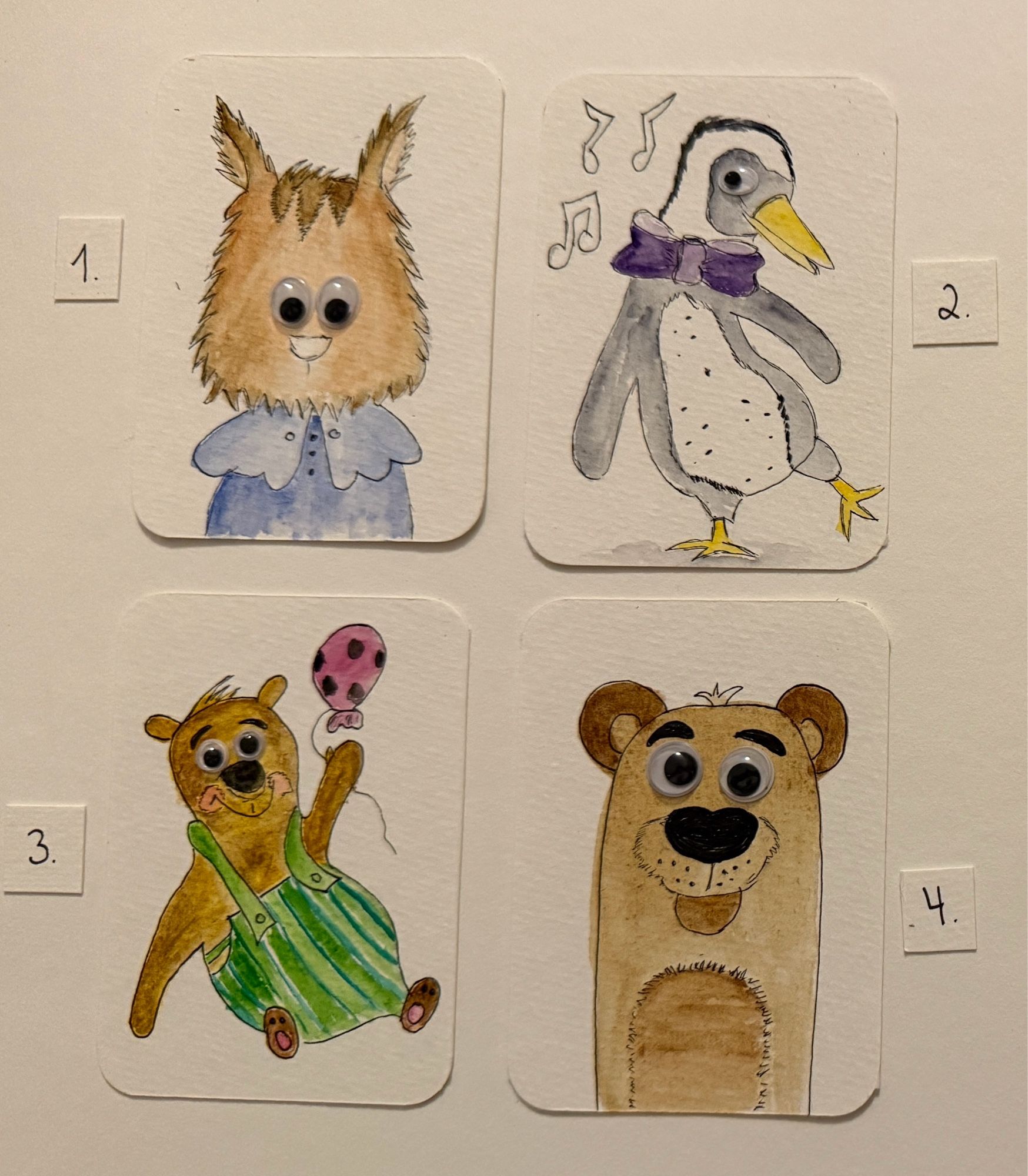 Vier ATC Hochformat mit Aquarellfarben bemalt und Wackelaugen. 
1) Hellbraune Katze mit blauem Kleid 
2) Tanzender Pinguin 
3) Bär in grün gestreifter Hise schwebt an einem Luftballon 
4) Brauner Bär