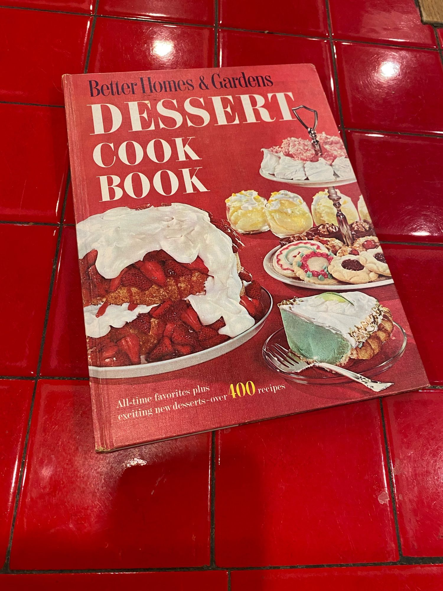 The cover of the Better Homes and Garden Dessert cookbook.  From bottom right clockwise: Americana Key Lime Pie, Strawberry shortcake, brownies, decorated sugar cookies, Cherry Winks, Jam Shortbread Cookies, divinity and coconut-coated marshmallows, lemon drop ice cream with marshmallow crème.