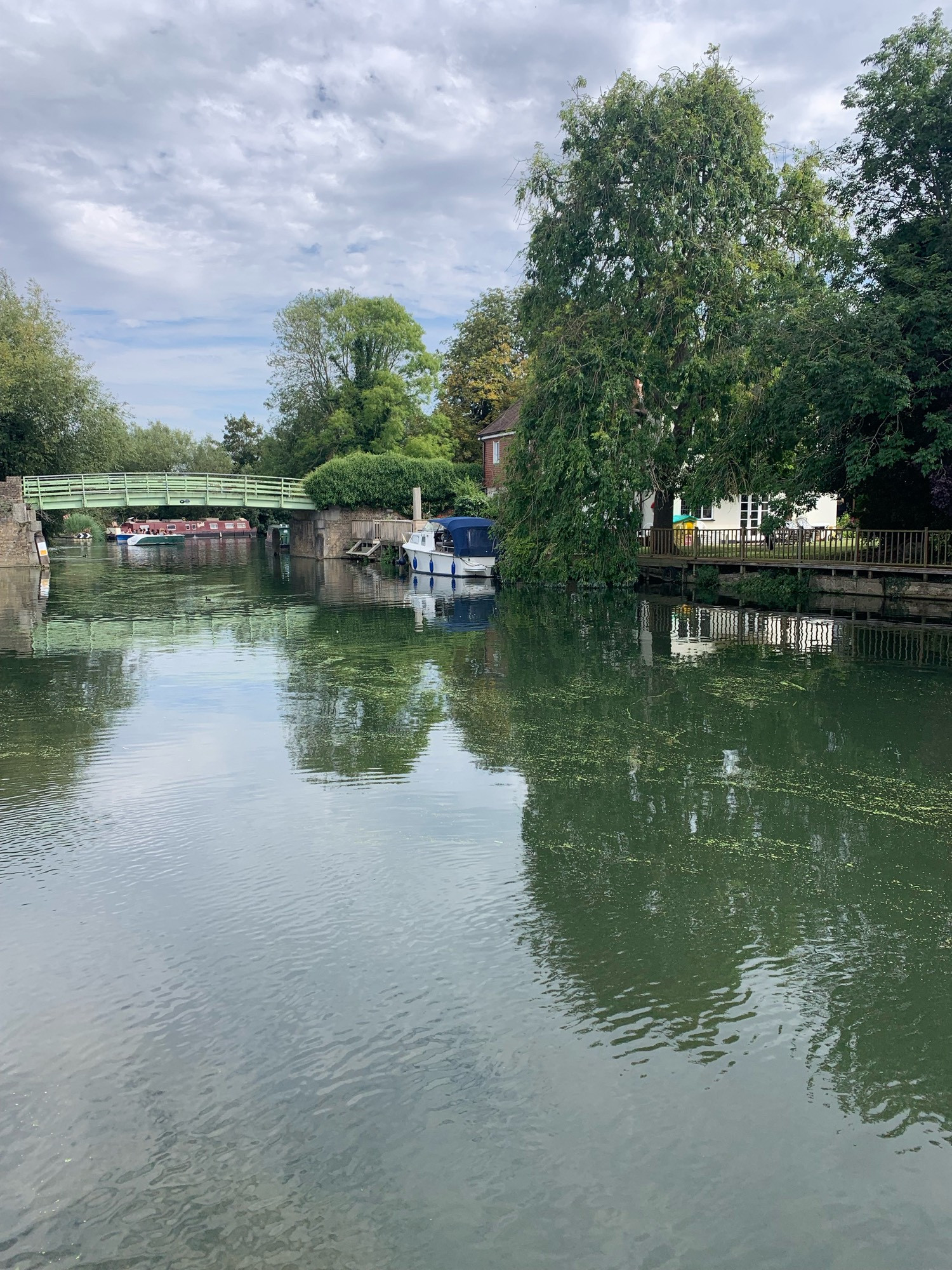 Canal with a green bridge across it in the distance. A boat is moored on one bank.