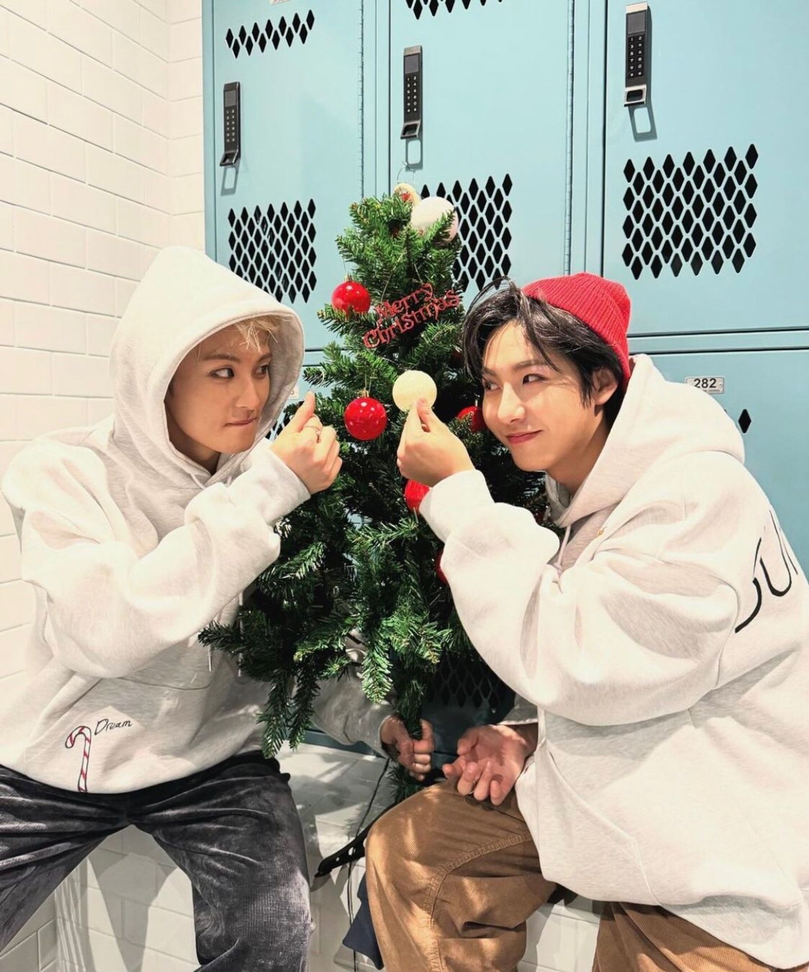 mark and renjun sending eachother finger hearts with a christmas tree between them