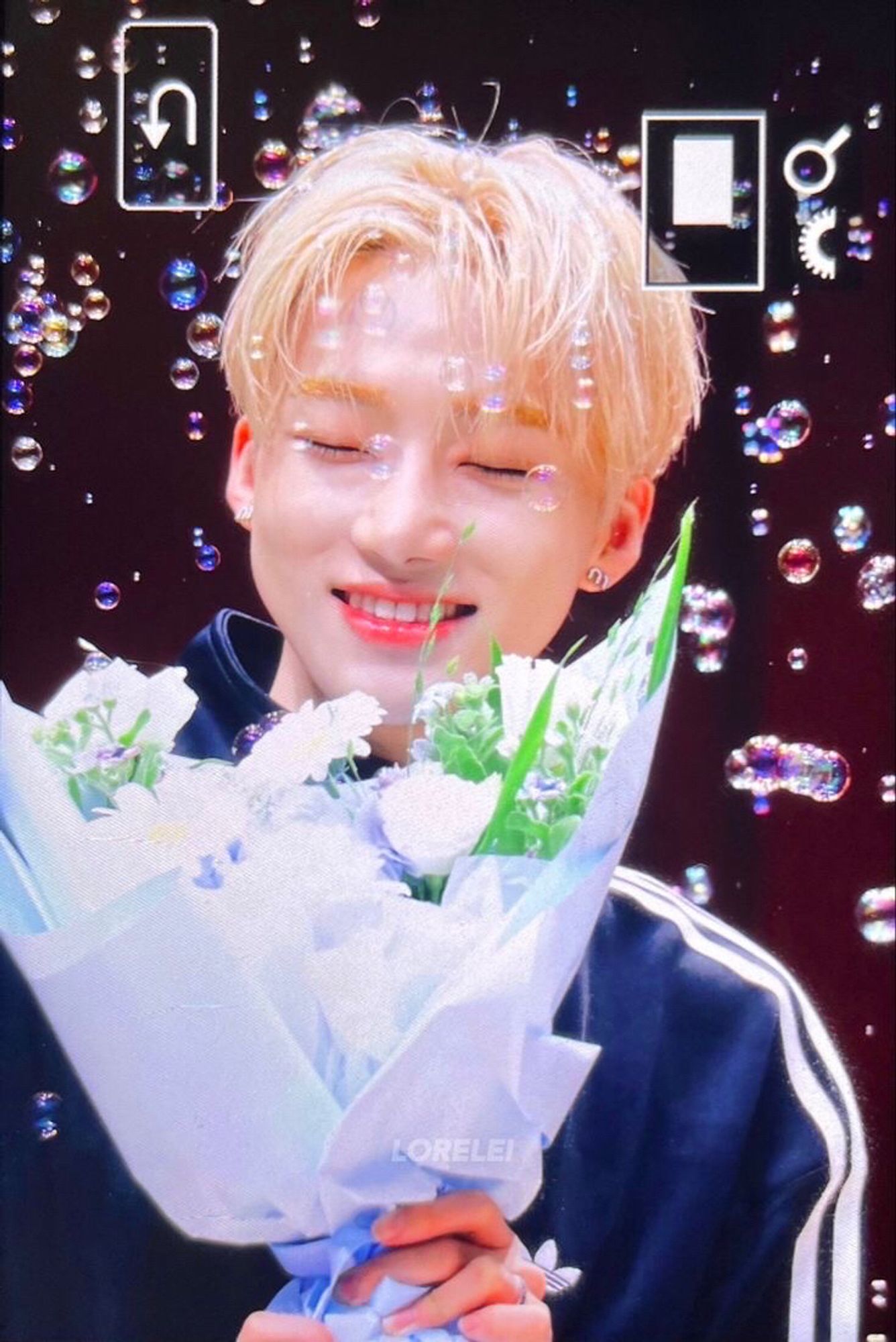 chanhee aka new smiling, holding a flower bouquet, while bubbles are flying all around him