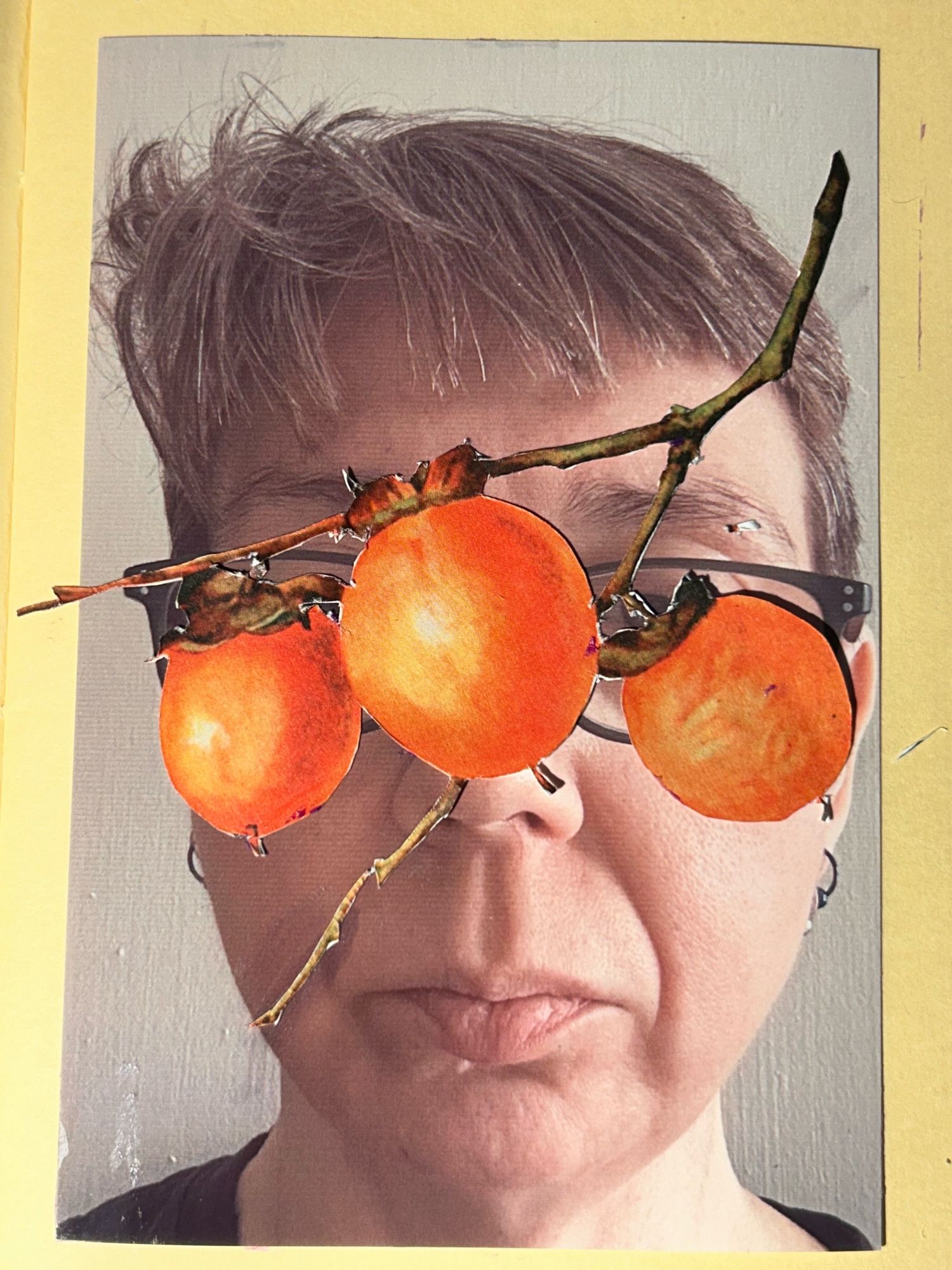 Photo of a white woman with short brown hair and dark rectangular glasses. In front of her face are a branch of three oranges, covering most of her eyes.