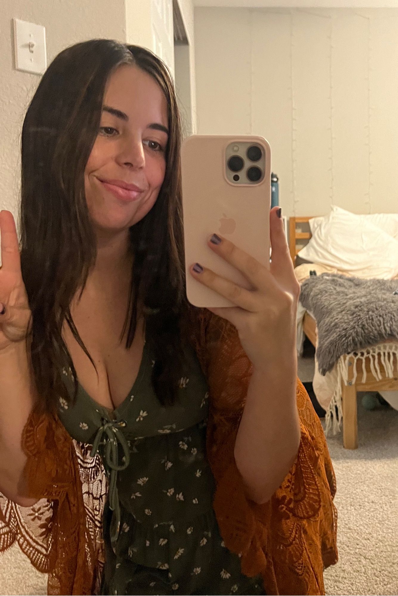 pic of me holding a peace sign up in the mirror. I’m wearing a low cut green dress with tiny white flowers on it, and an orange lace cardigan over it