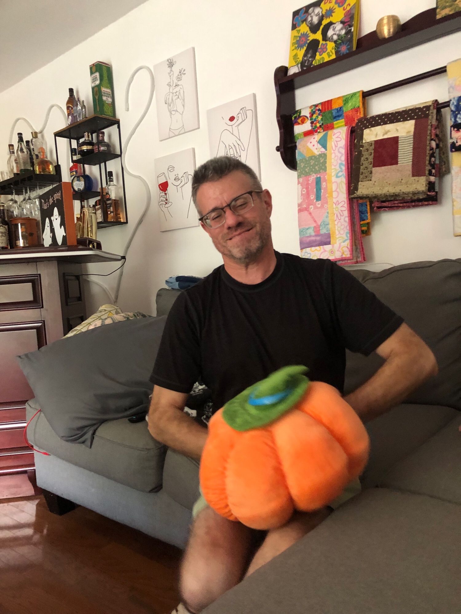 A middle aged man sits on a sofa with a stuffed pumpkin on his lap. Both of his hands are inserted inside the pumpkin