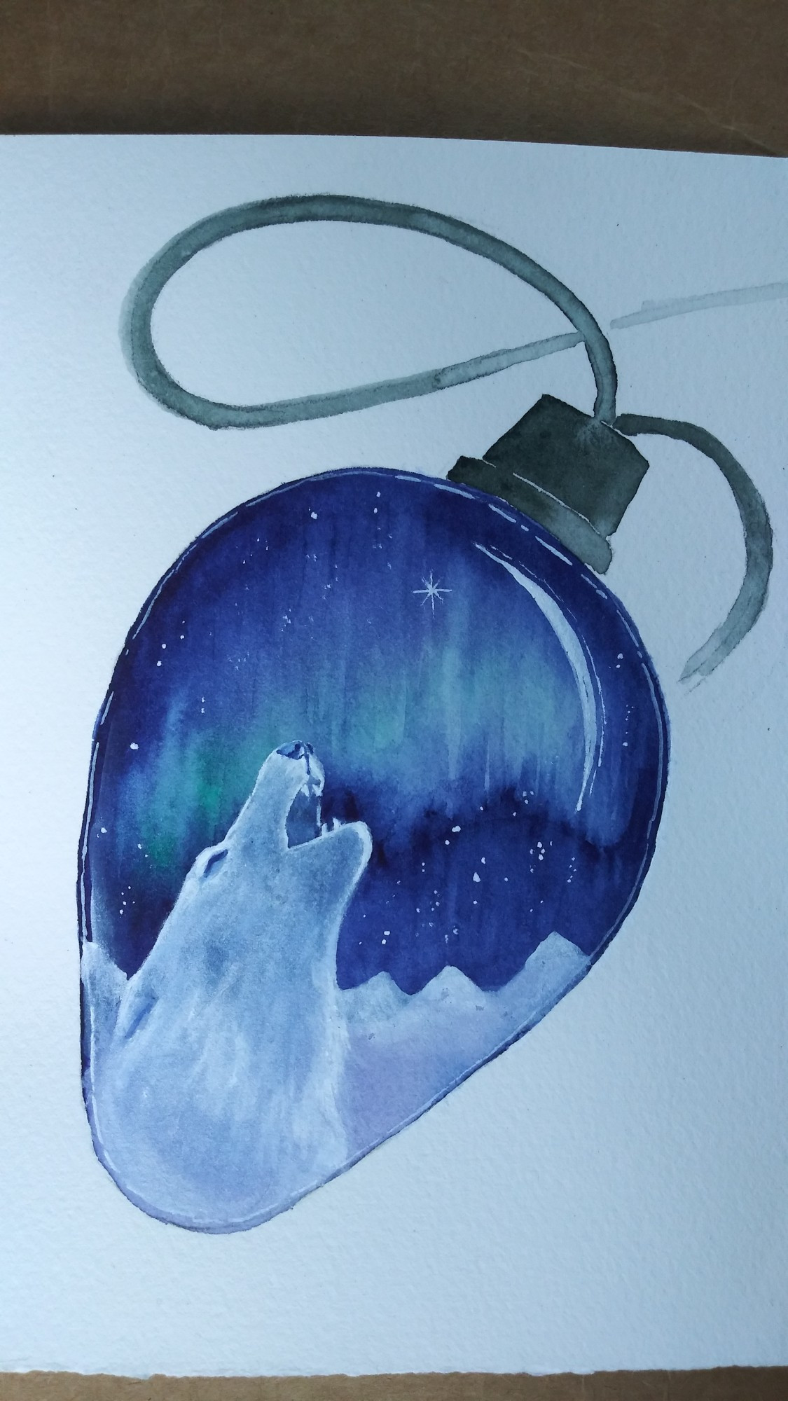 A watercolor holiday card. It has a white background, with a painting of a clear C-7 Christmas light bulb. The bulb is elongated and wider at the top, where a green cap shows a short bit of the cord that would make up the light string. Inside is a small scene featuring a green aurora in a winter night sky. Deep indigo frames a green curtain of northern lights and many stars. At the horizon, a distant mountain range is covered with snow. In the foreground, we see the head and shoulders of a white wolf howling into the night. Painted highlights remind us we are looking into a glass bulb. Card is approximately 4" x 6" and made of 140lb watercolor paper, painted with watercolor and gouache.