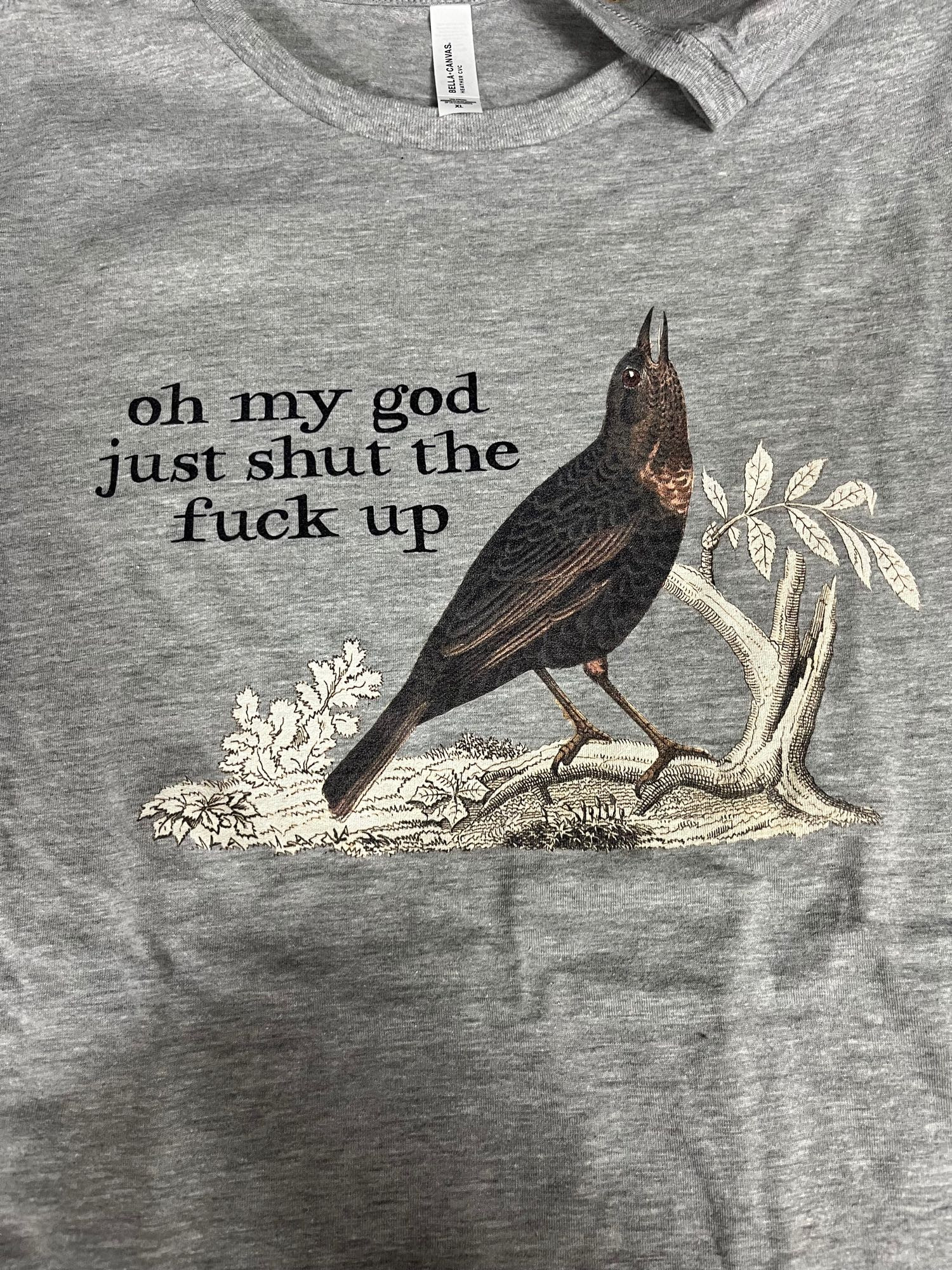 A t-shirt with a picture of a bird that says “oh my god just shut the fuck up.”