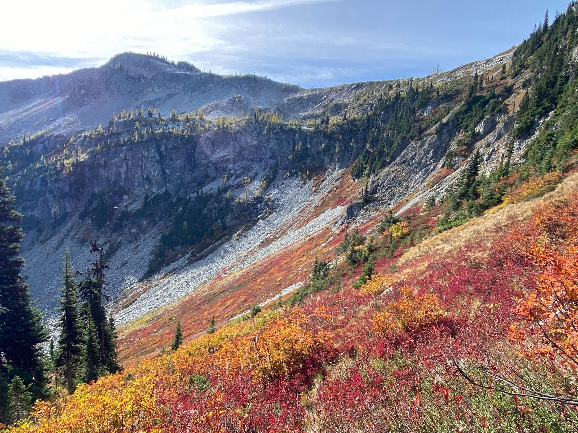 Amazing orange, red, and yellow fall foliage at Maple Pass in WA. If you look closely you can see yellow larches in the background, above a steep scree slope.