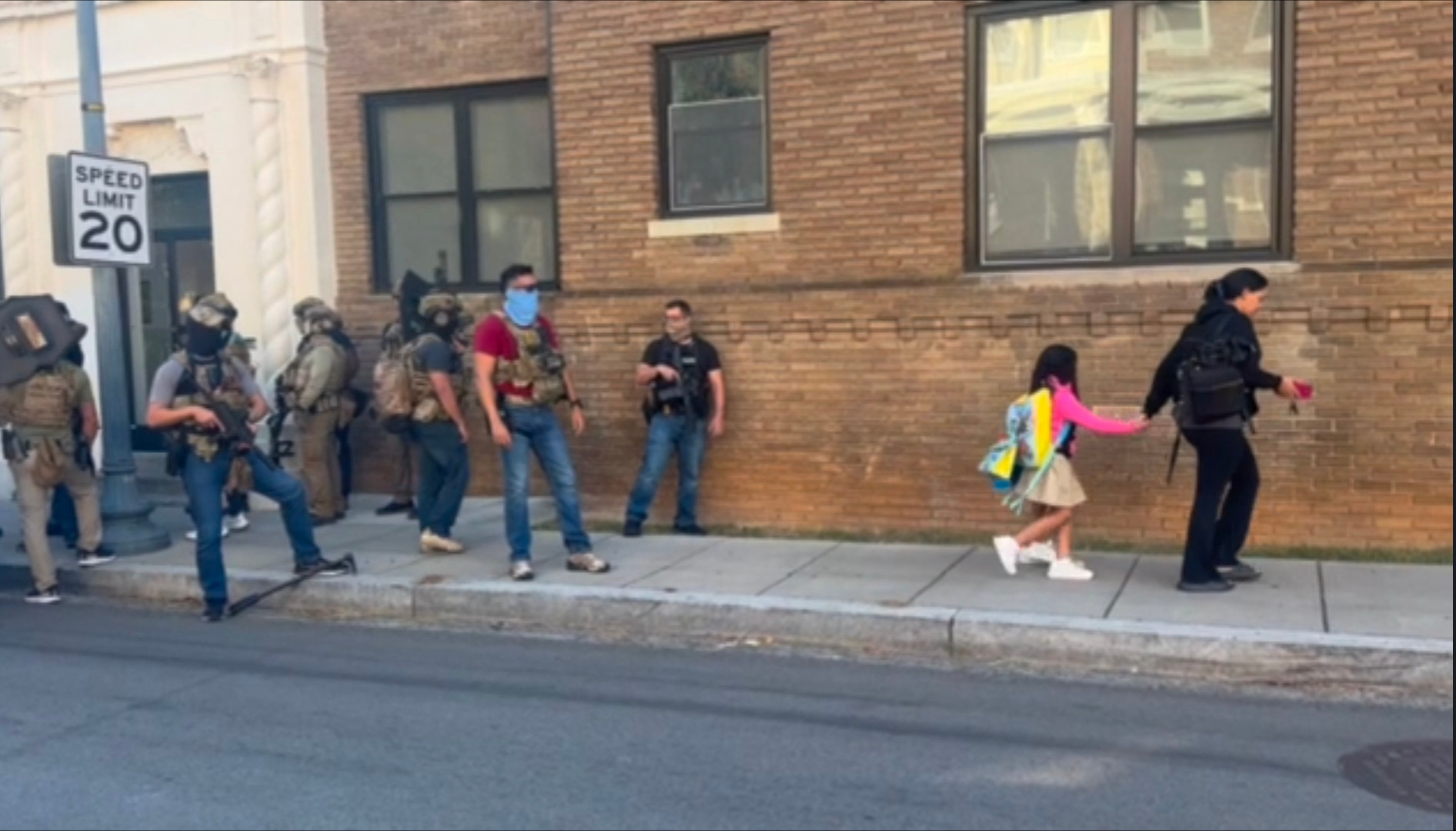 Masked armed men watch a mother and her children go to school.