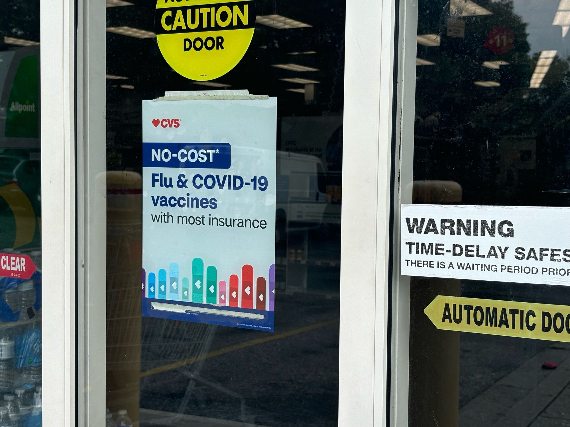 CVS entrance door with a sign stating “No-cost* Flu & COVID-19 vaccines with most insurance”