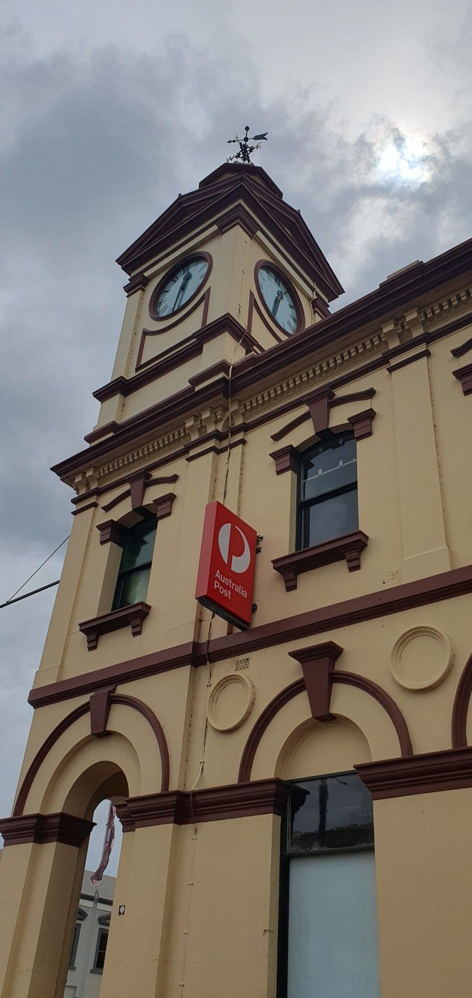 1900s clock tower with modern 'Australia post' sign on it