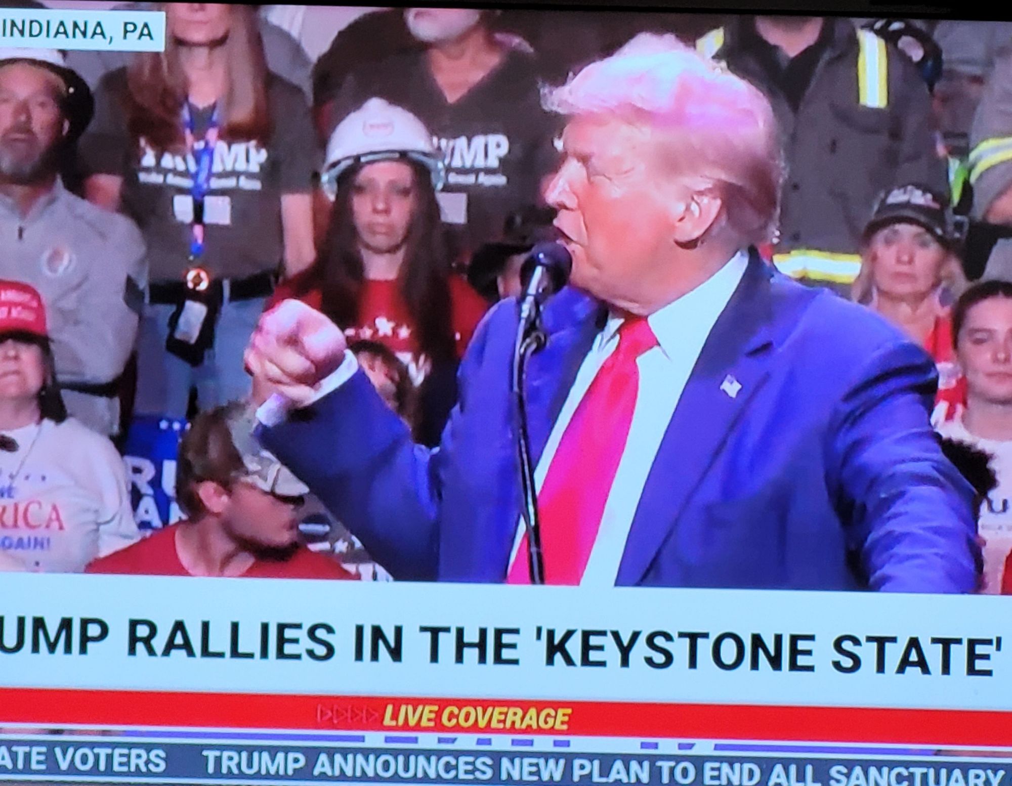 Trump at a lectern looking sideways. His hair looks pink.