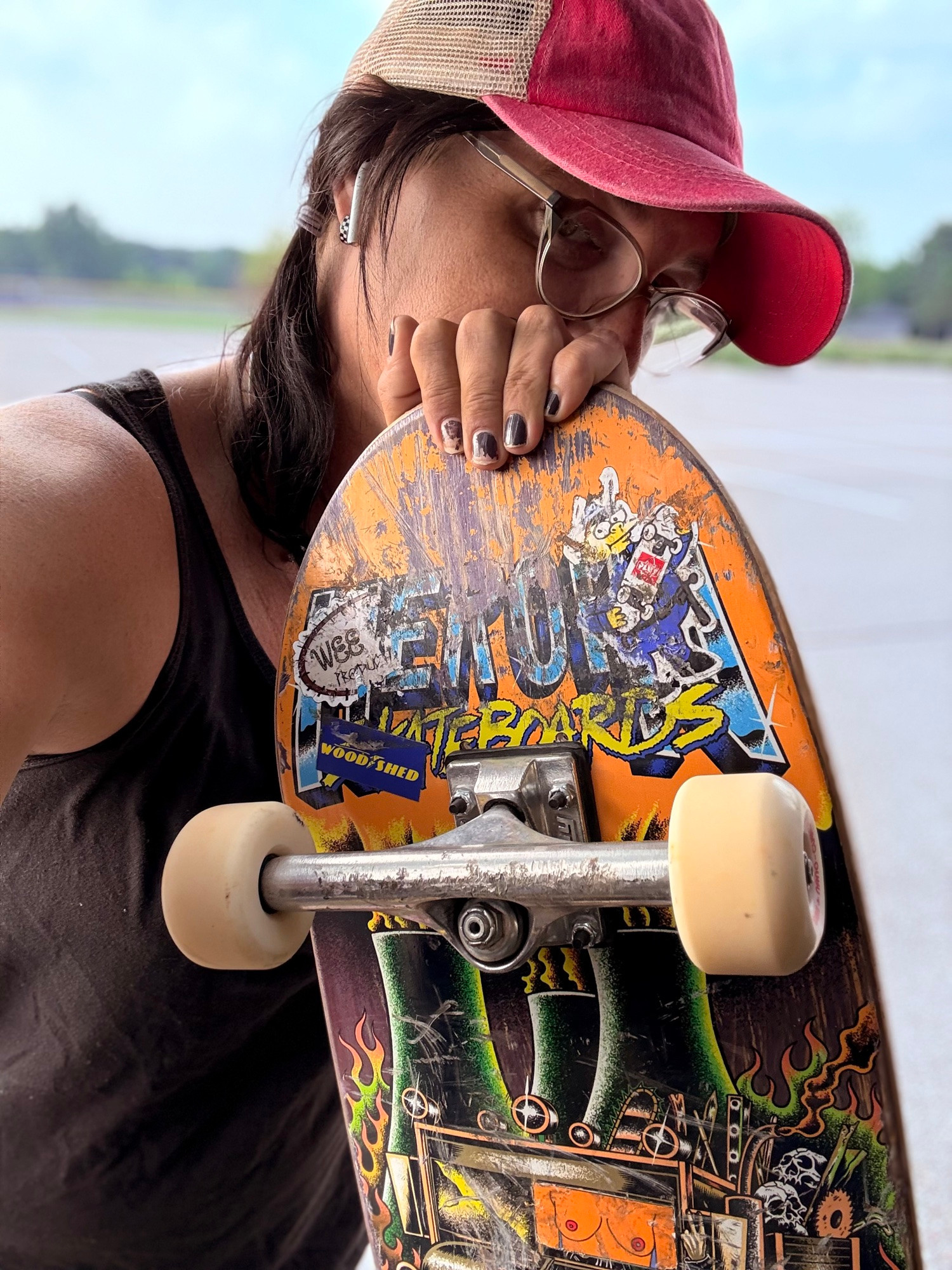 daffodil in a black tank top, same pink baseball cap, but most of her face is obscured by her skateboard, which is all scraped up from doing tricks and fallen. There’s a few stickers on the nuclear power plant theme deck that she has.