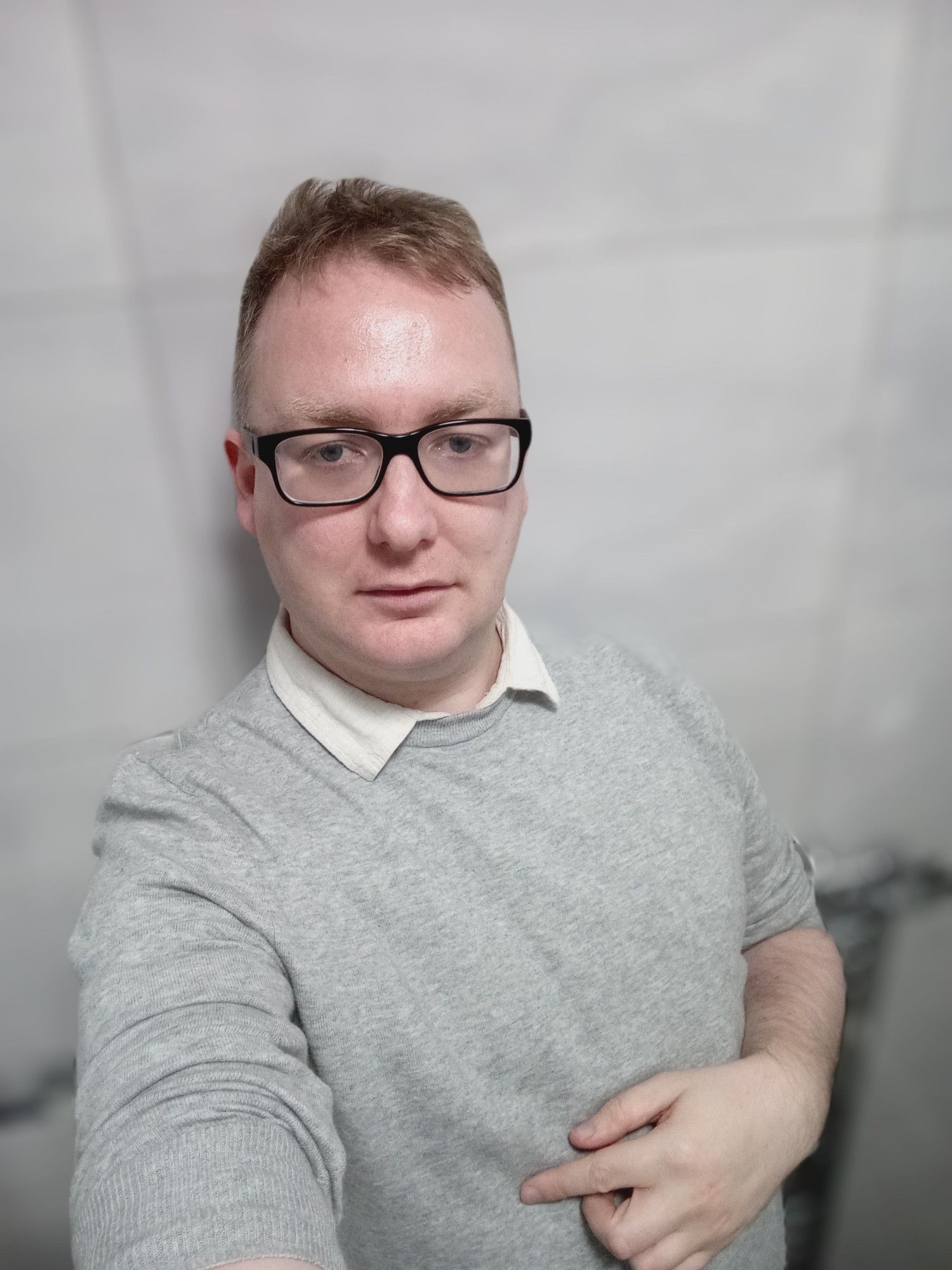 Me, bespectacled white blond non binary person in a grey jumper, dark grey jeans and white collar, standing in a bathroom selfie photo