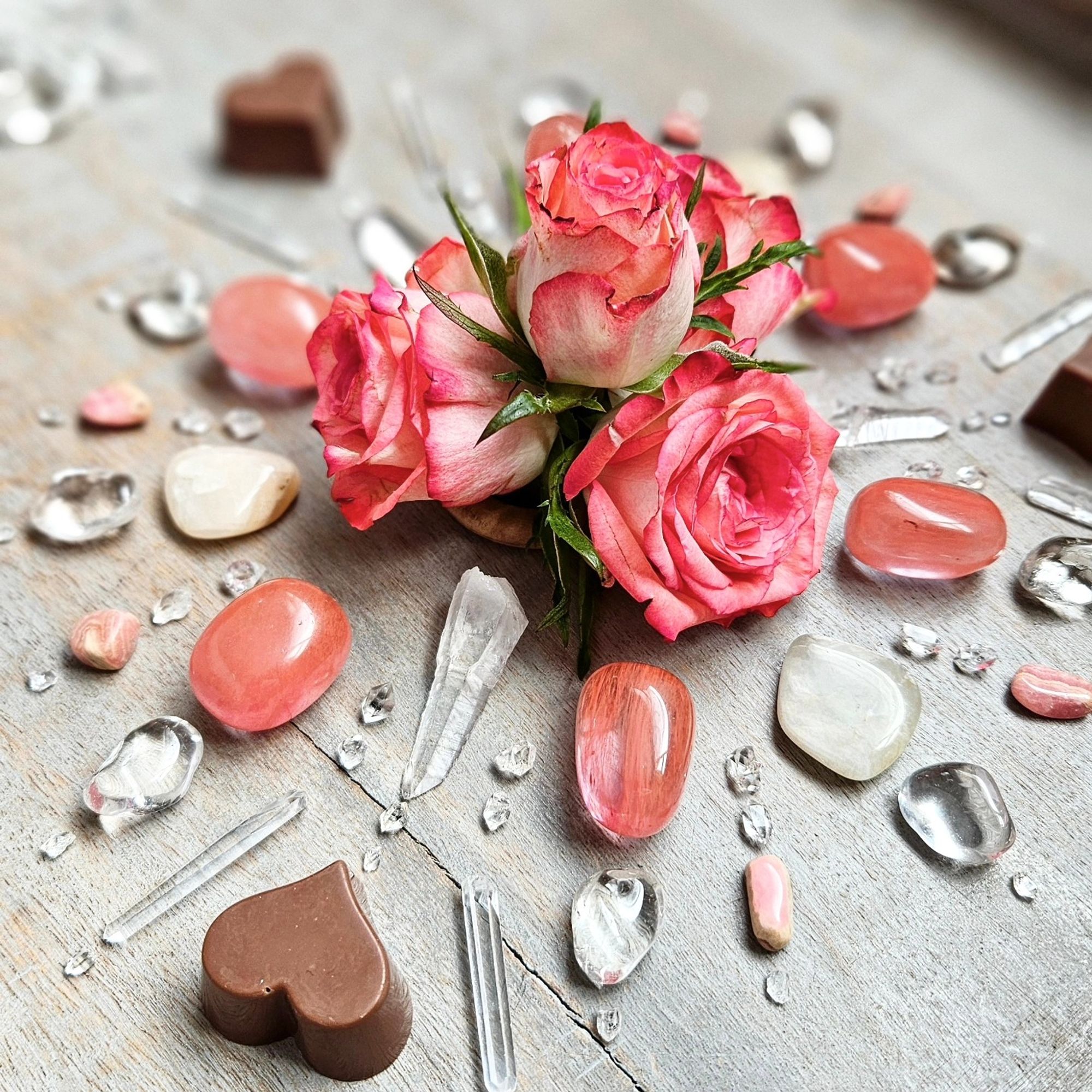 Different angle of crystal grid, with roses off centre, showing the left side of the grid with Cherry Quartz, Moonstone, Clear Quartz points and stones, Rhodochrosite, Herkimer Diamond, and chocolate hearts.