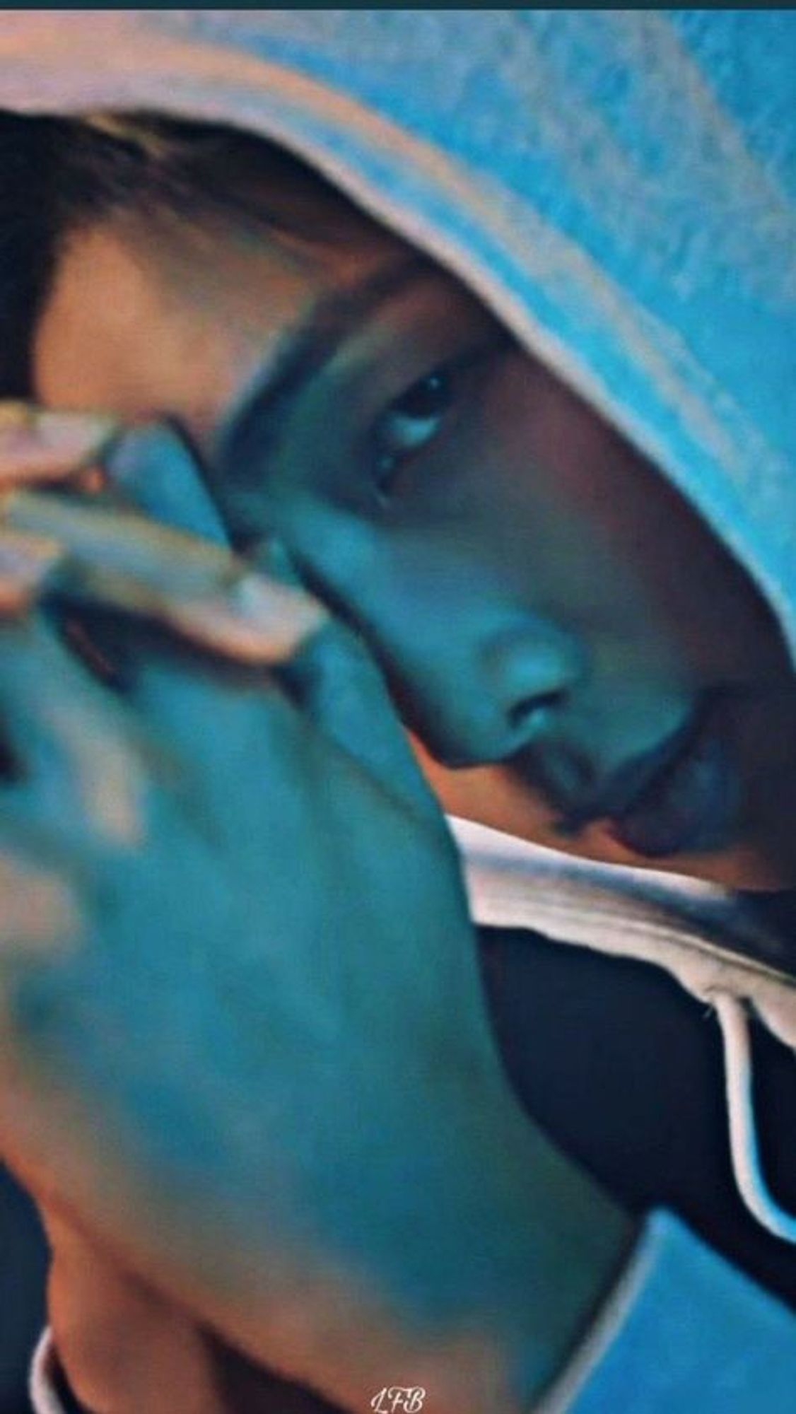 Namjoon in a hoodie, facing left, and glancing at the camera as though he has been disturbed in something private. The heavy blue and gold contrast lighting makes him look much more menacing than he actually is.