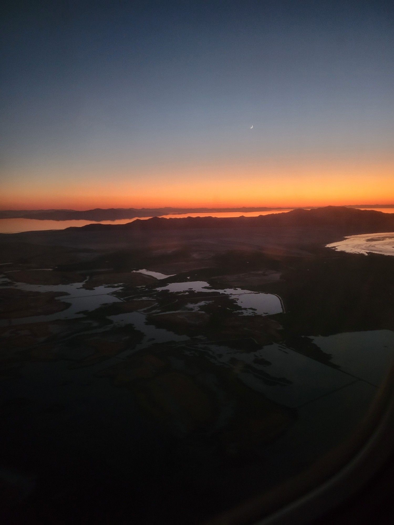 A view of the sunset and the moon from an airplane window.