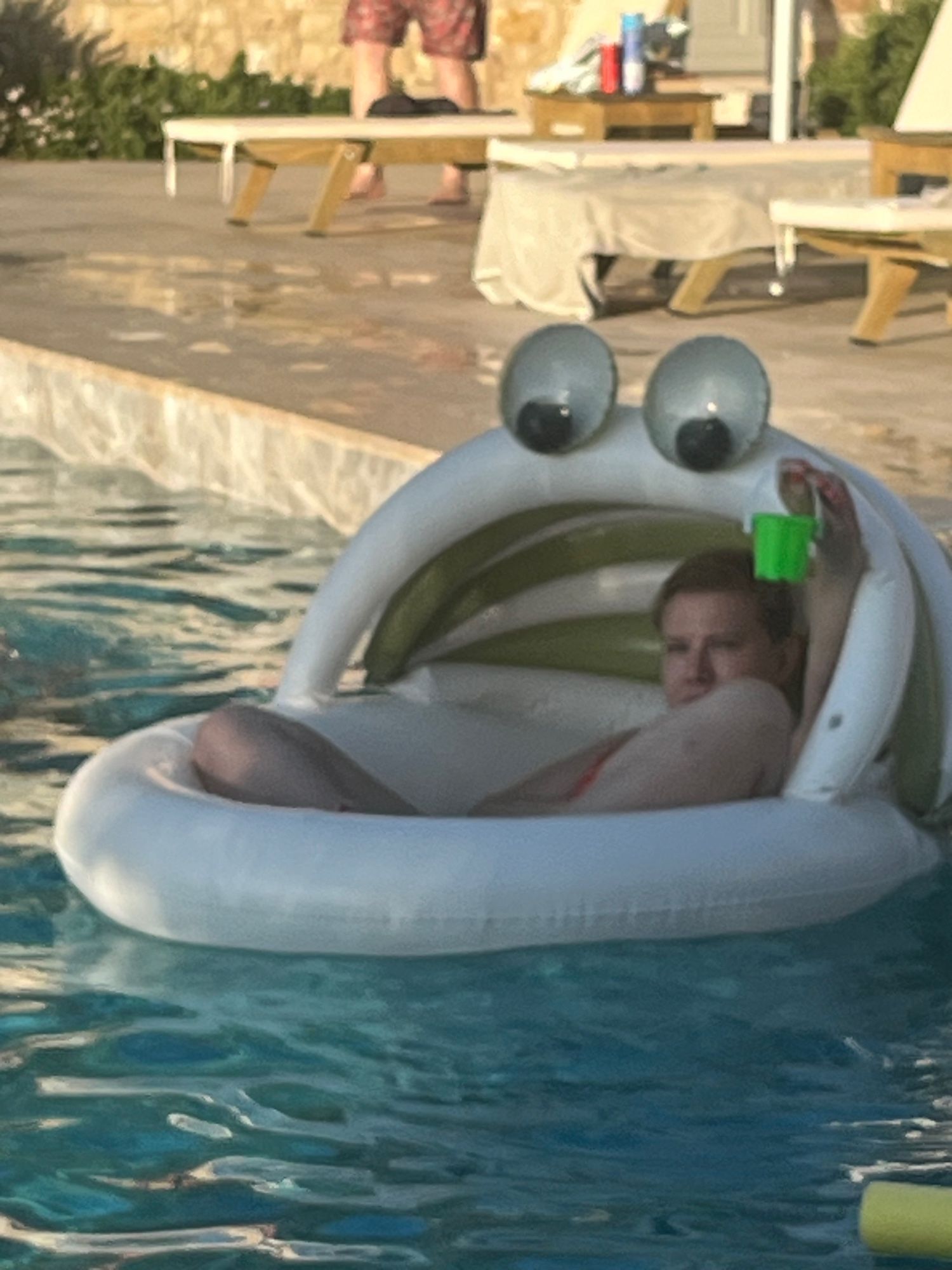 Picture of me floating in an inflatable with a cover- like a bassinet with googly eyes on top. I’m folded inside it looking vaguely grumpy, and holding up a tiny green bucket. The picture is weirdly grainy.