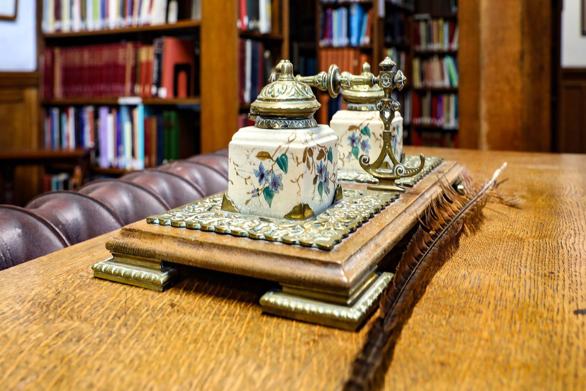 A set of painted ink pots on a stand on a desk in the Reading Rooms. A pheasant feather sits next to them. It looks like a quill.