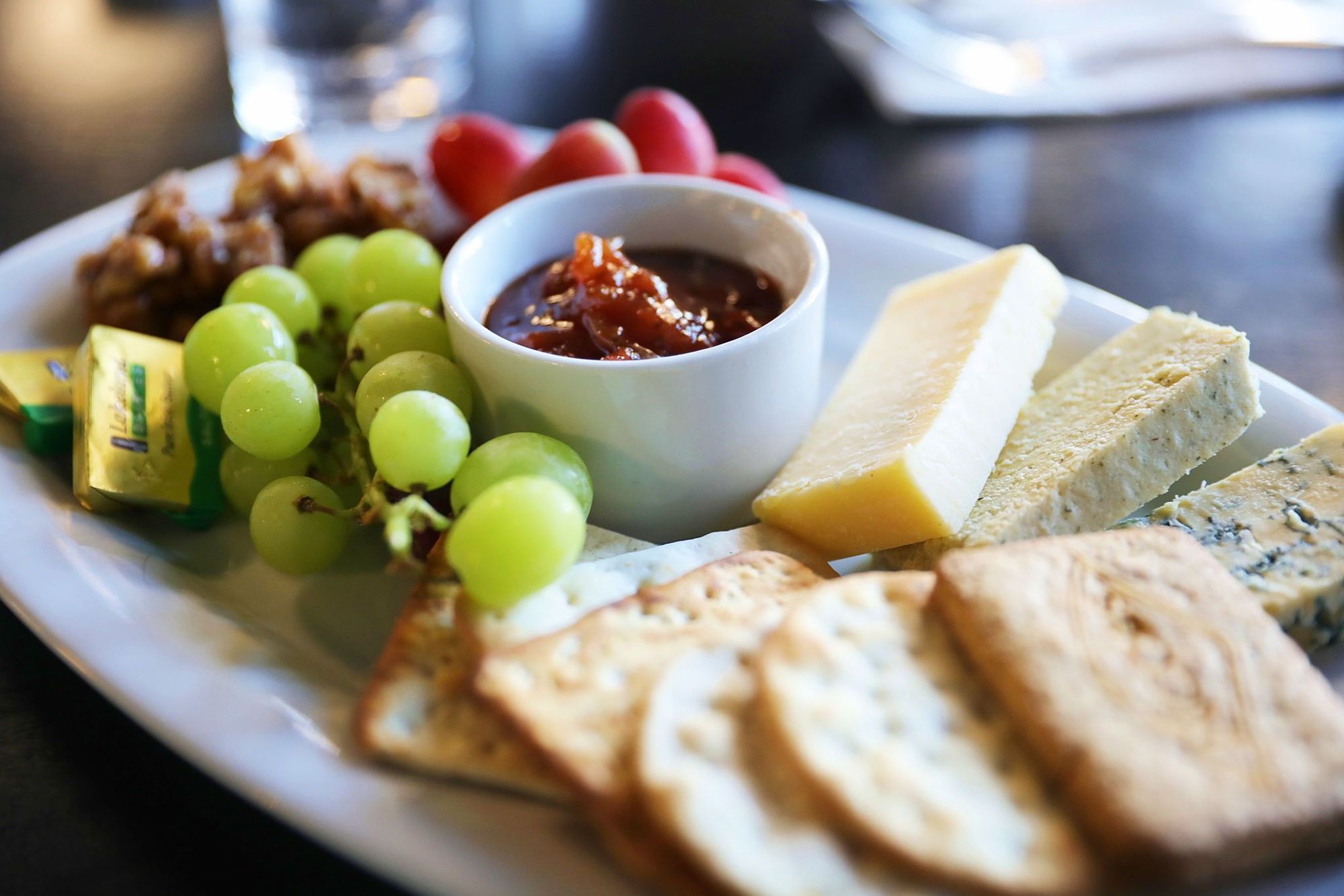 A platter of cheeses with crackers, grapes etc as described in the main post, arranged on a long, white plate