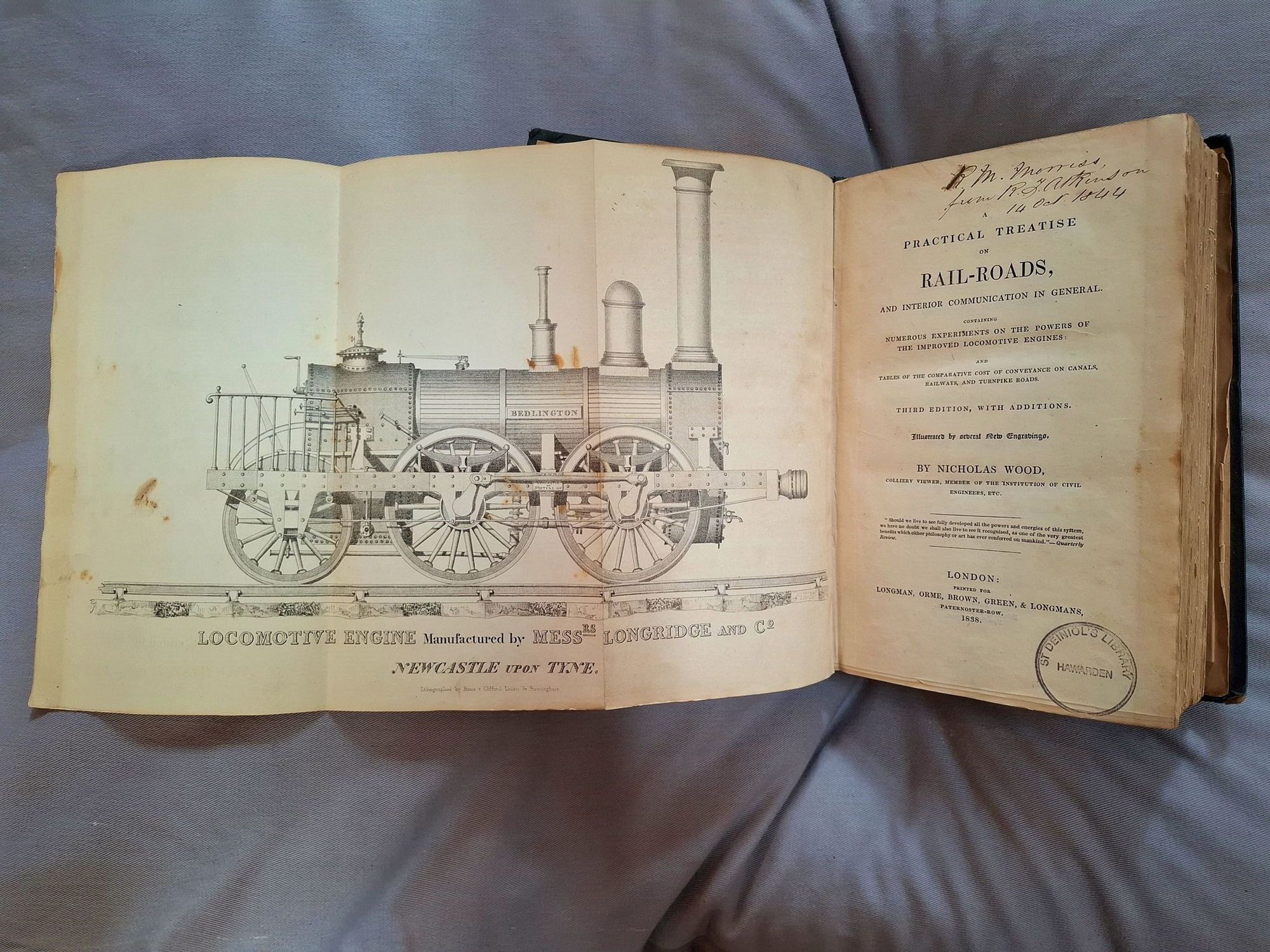 A book on a grey cushion. It is open and one of the pages has opened out to show an ink diagram of a steam train