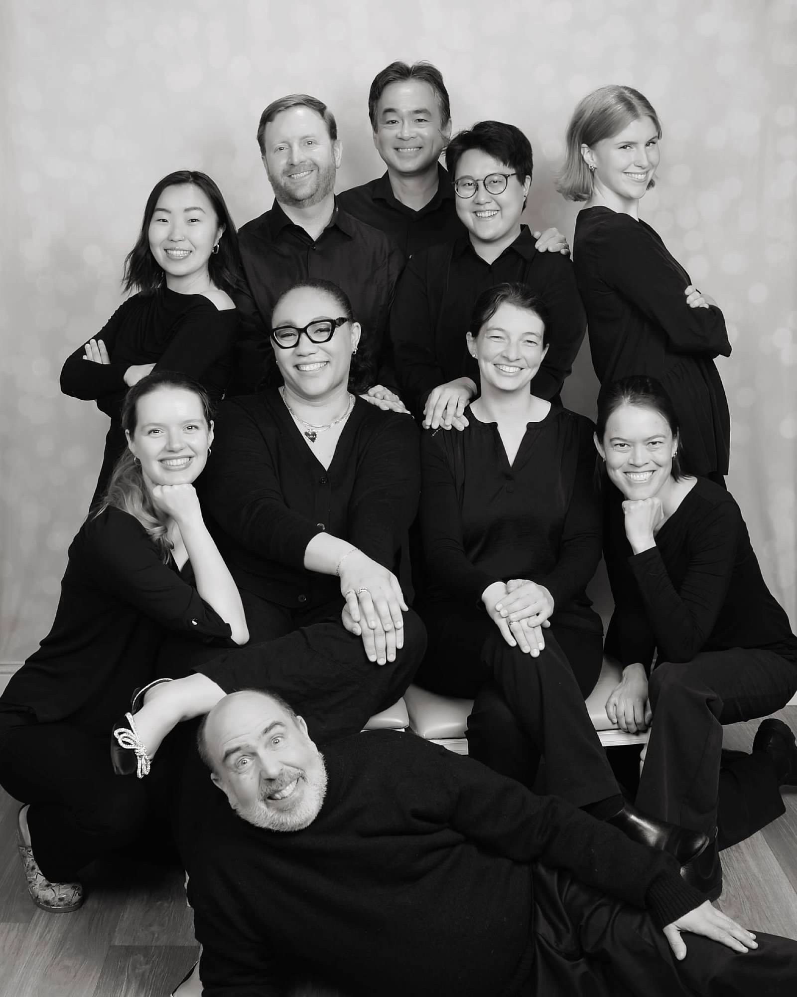 The same ten violists, only this time in a vaguely professional black and white group shot that looks like it might be a cast photo from a 1980s TV sitcom. All are smiling normally except for the one called Ken, who is lying sideways in front of the group like a pinup model. Everyone is smiling nicely except for Ken, who is smiling like a serial killer.