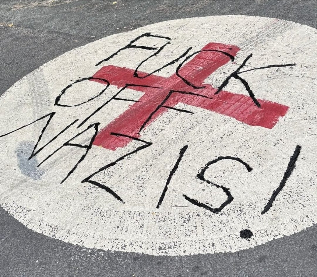 A roundabout with a George Cross painted on it. Somebody has written "FUCK OFF NAZIS" across it. Apparently photographed in Leeds 