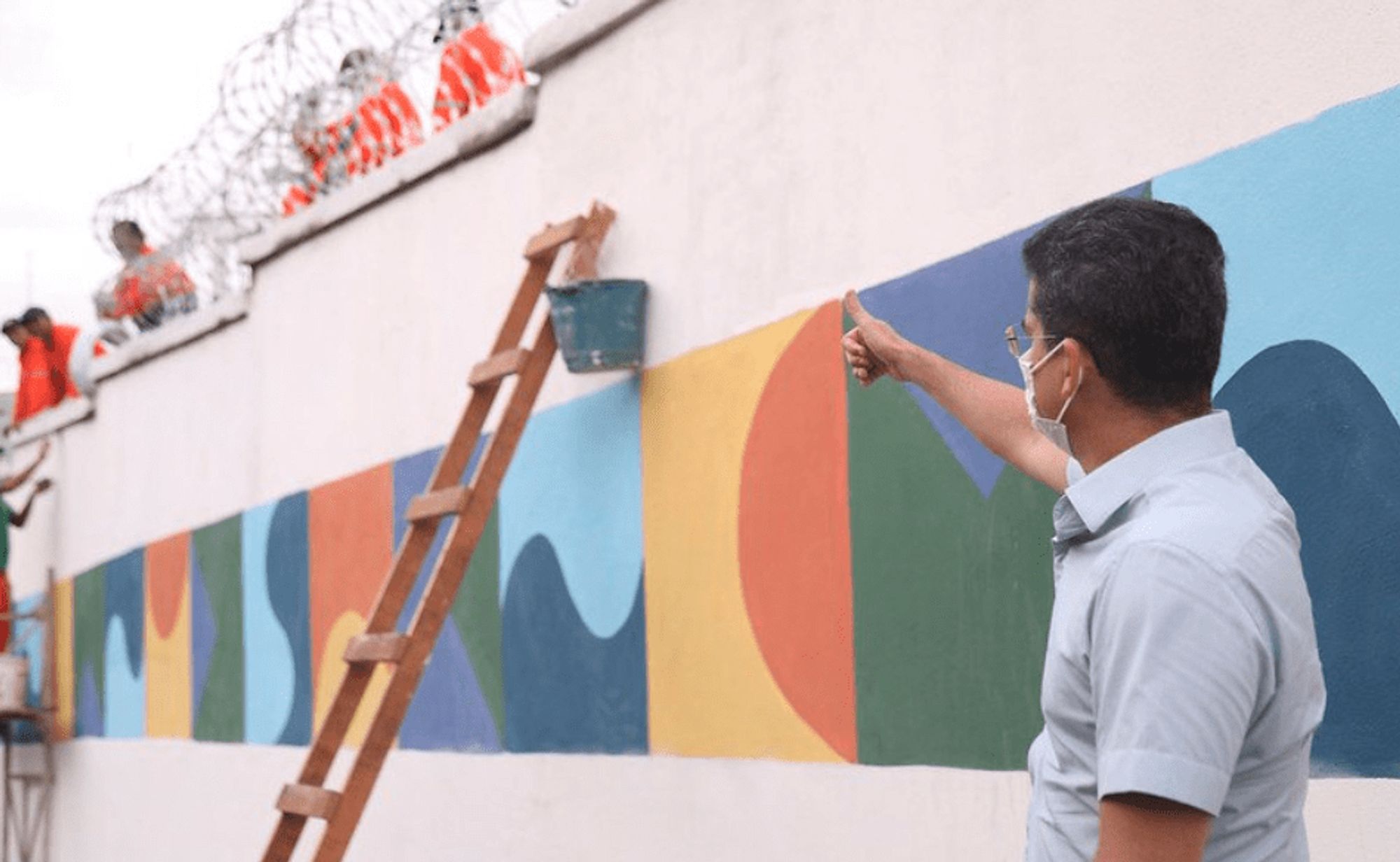 O prefeito de Manaus dando um joinha pra um muro pintado com a identidade visual da prefeitura.