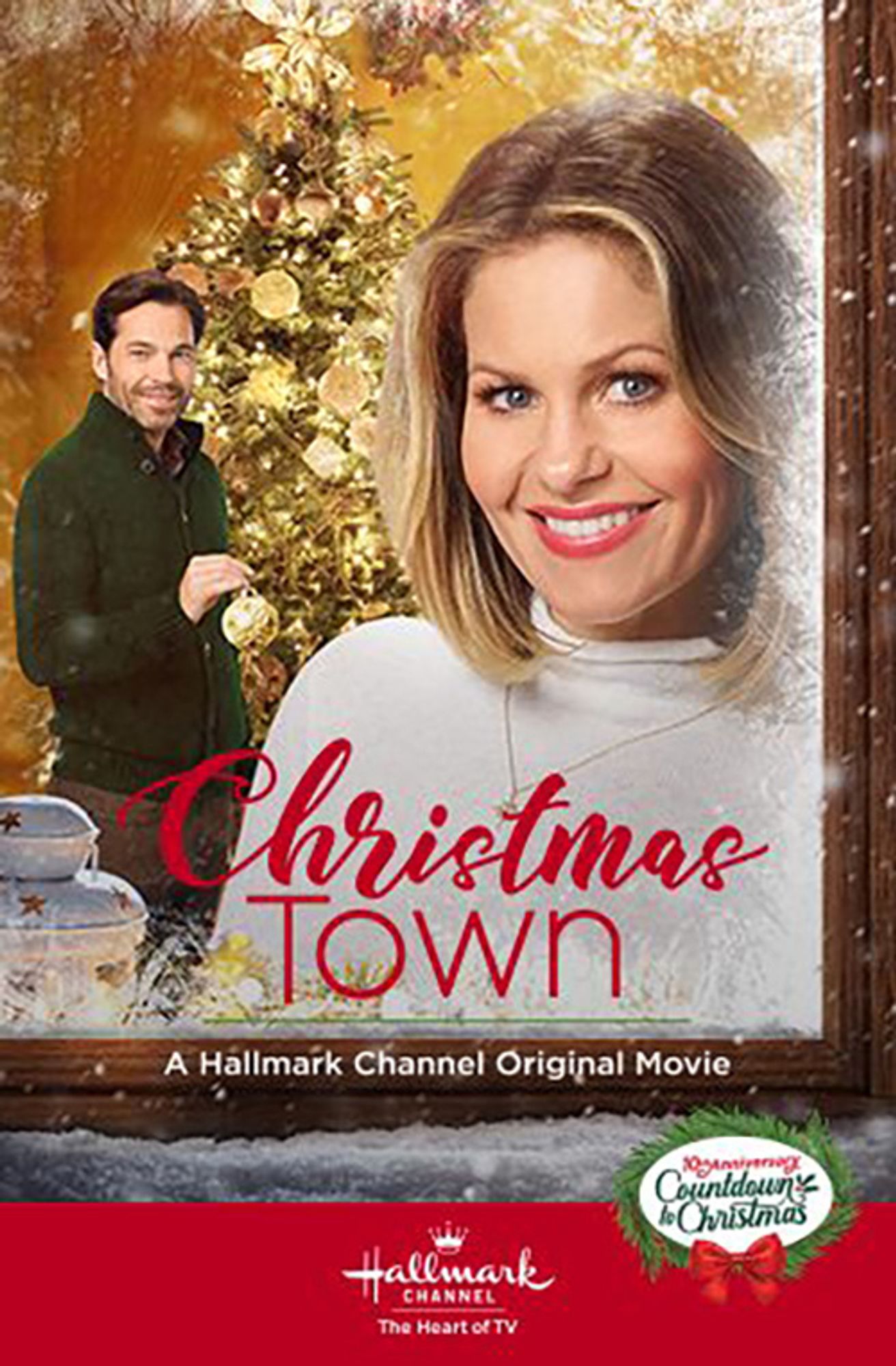 Christmas Town promo image. Candice Cameron is in the foregound, wearing a white sweater and staring out a window towards the viewer. Mutt is standing behind her in a green sweater also looking towards the viewer while holding a white tree ornament. Title in red on the bottom. Hallmark logo in red and white below the the title.