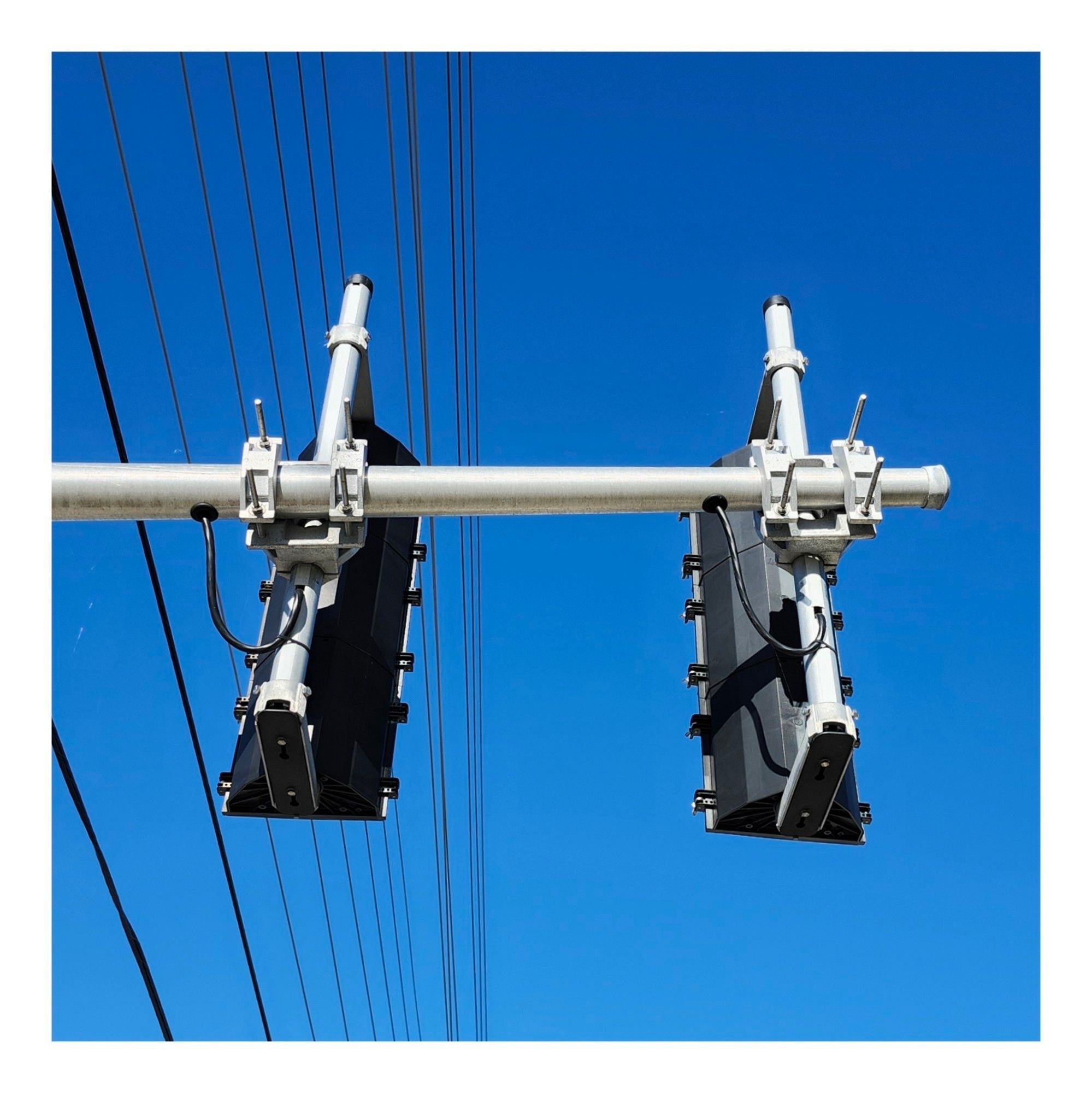 The rear of two bicycle traffic lights underneath power lines and a blue sky in Mississauga Ontario