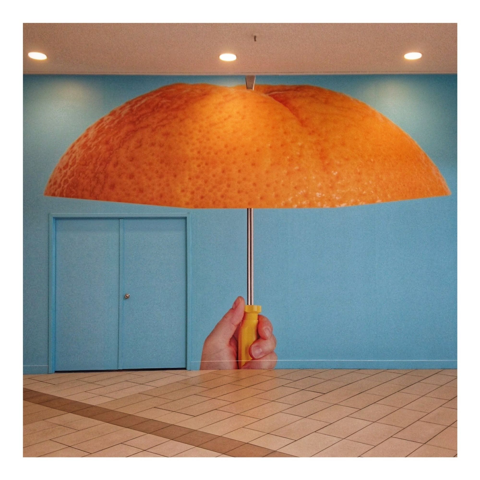 Blue hoarding in front of a closed storefront showing an umbrella made of the top of an orange, suggesting that the mall it appears in will be able to sell you both oranges and umbrellas. ellas. ellas. eh. eh.