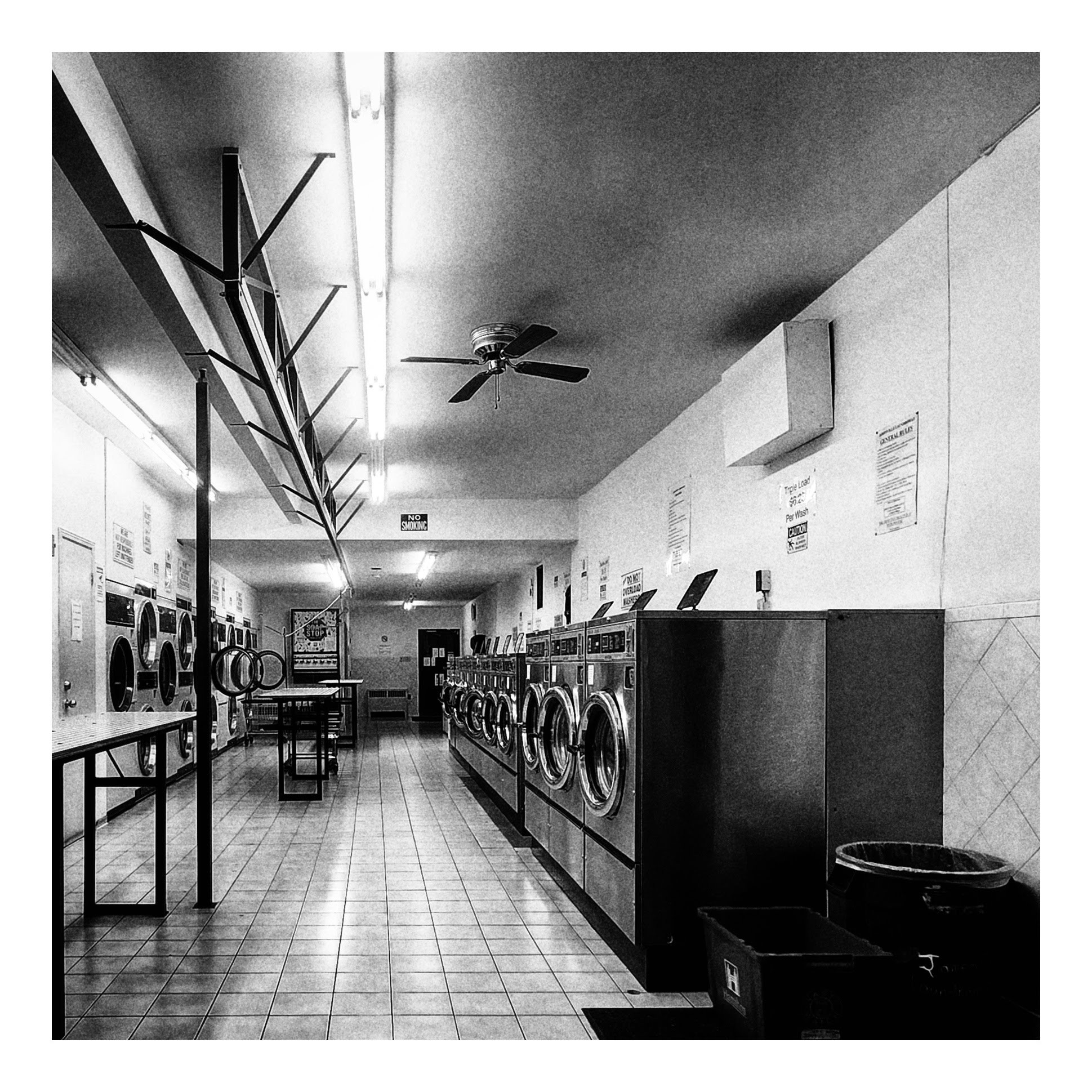 The interior of an empty laundromat with washers on the right, dryers on the left and folding tables down the middle