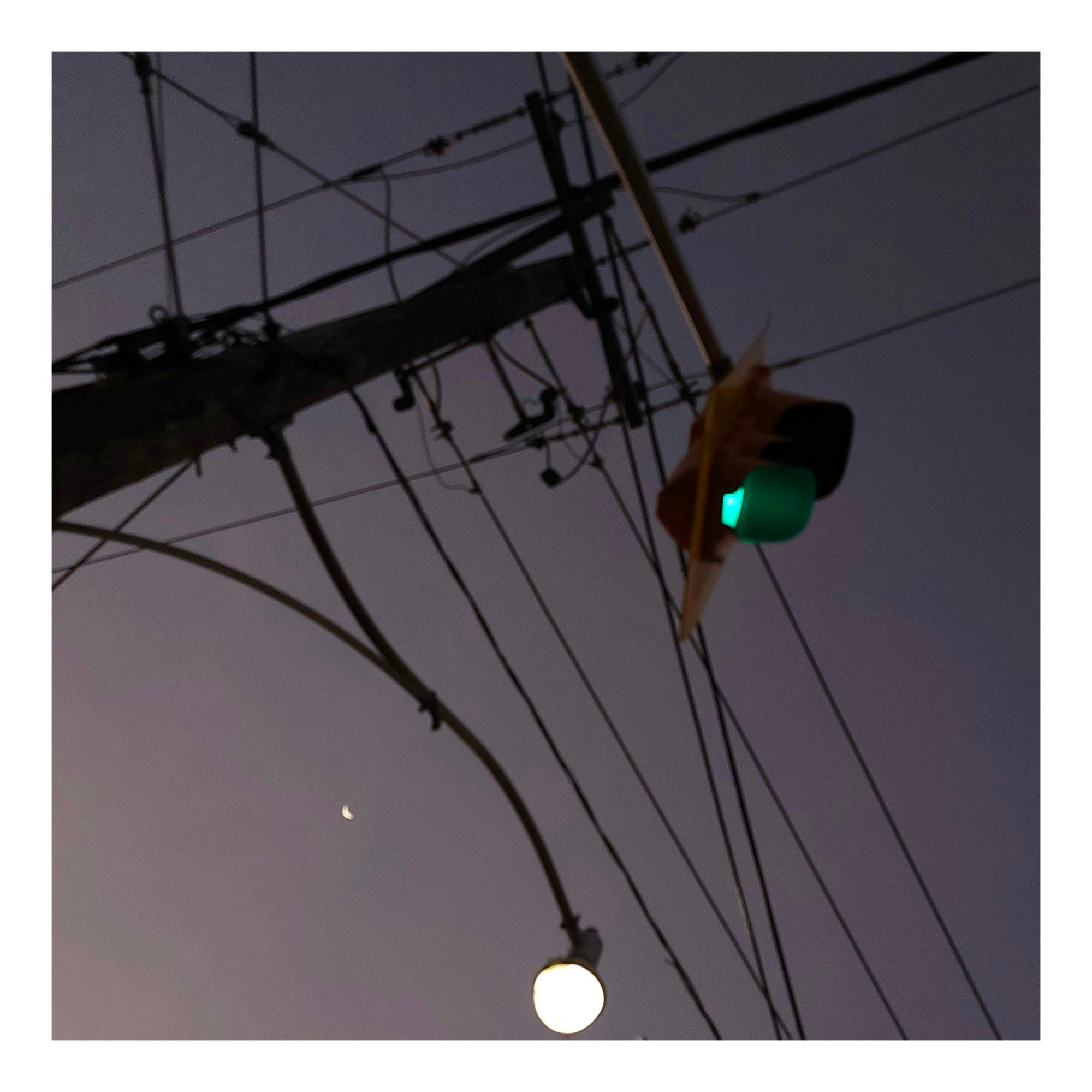 A crescent moon, street light, stoplight and various power lines over Queen Street East in Toronto Ontario