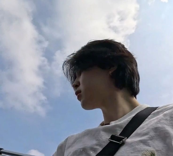 A photo of BTS's Jimin getting out/in a car, he wears a white t-shirt with a side bag and in the background is a sky full of clouds. (Content taken from the program "Are You Sure?!")