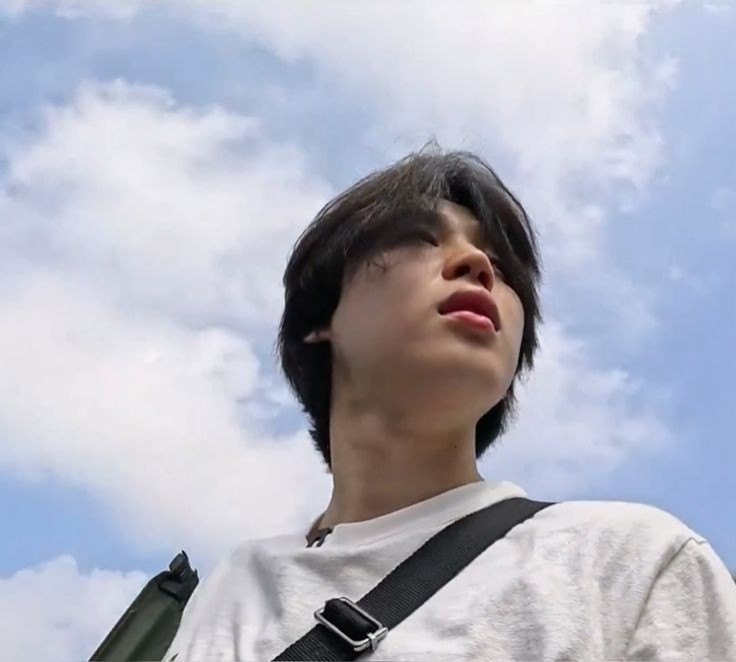 A photo of BTS's Jimin getting out/in a car, he wears a white t-shirt with a side bag and in the background is a sky full of clouds. (Content taken from the program "Are You Sure?!")