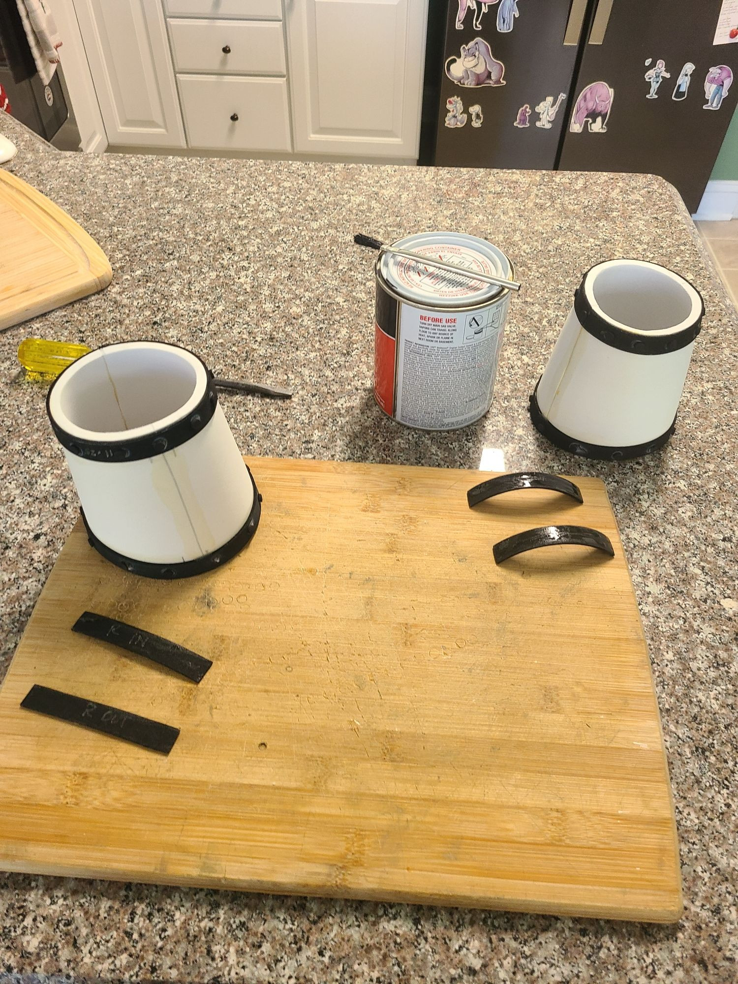 A foam bracer with two strips of black foam glued up and ready to attach. These will be covered with rivets of foam, but are really just to hide the seams. Another bracer is in the background but the foam strips are curved backwards from the glue, and show a wet shine