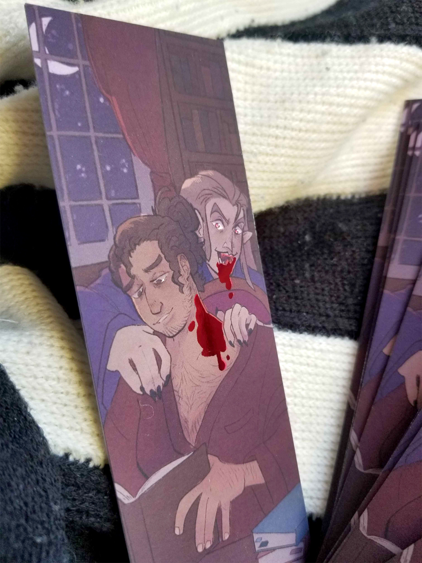 A close-up of one of the bookmarks showing some of the detail of the contented face of the human and grin of their vampiric predator.