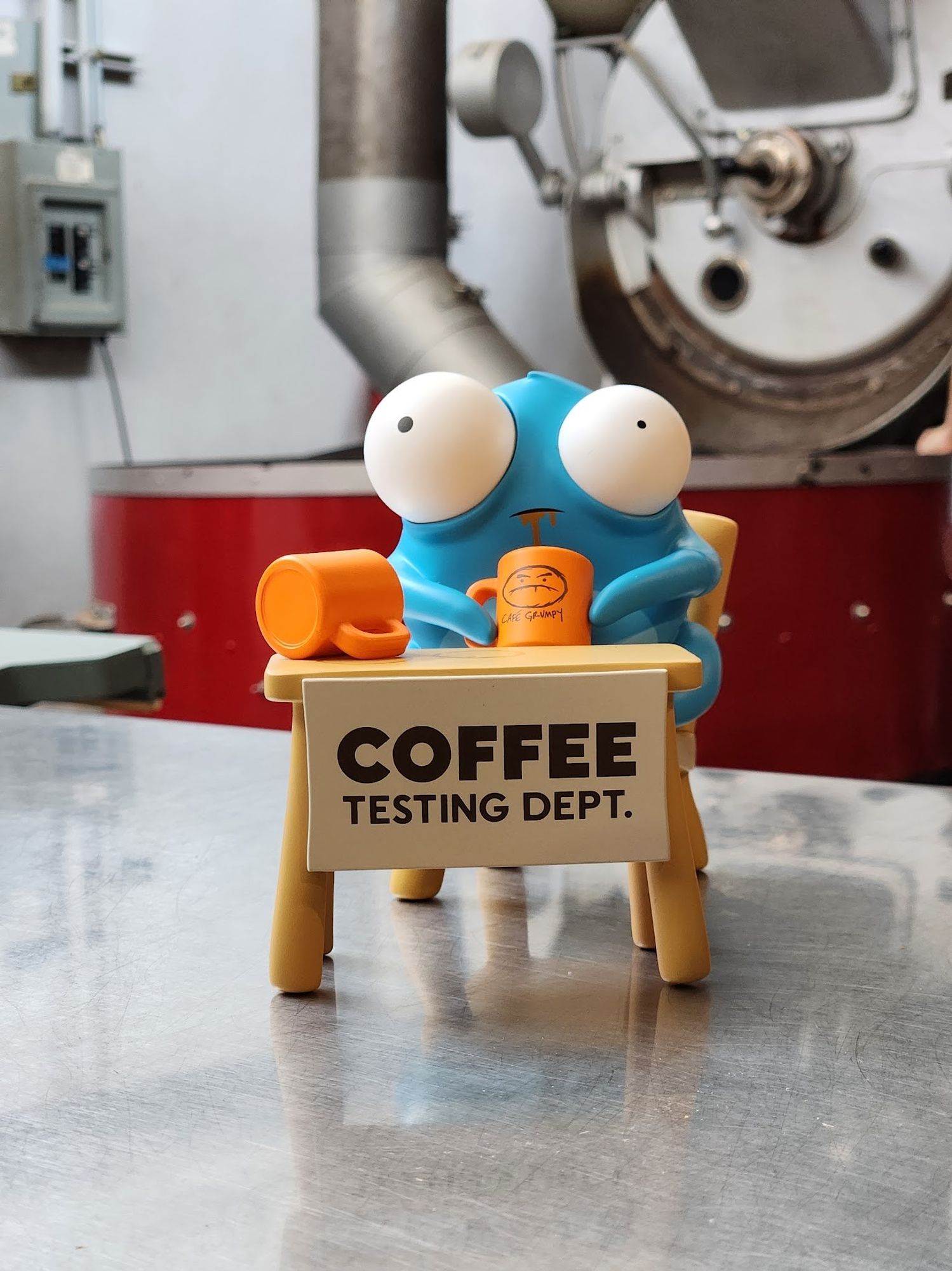 photo of Coffee Testing Dept figure on steel table in front of PROBAT roaster