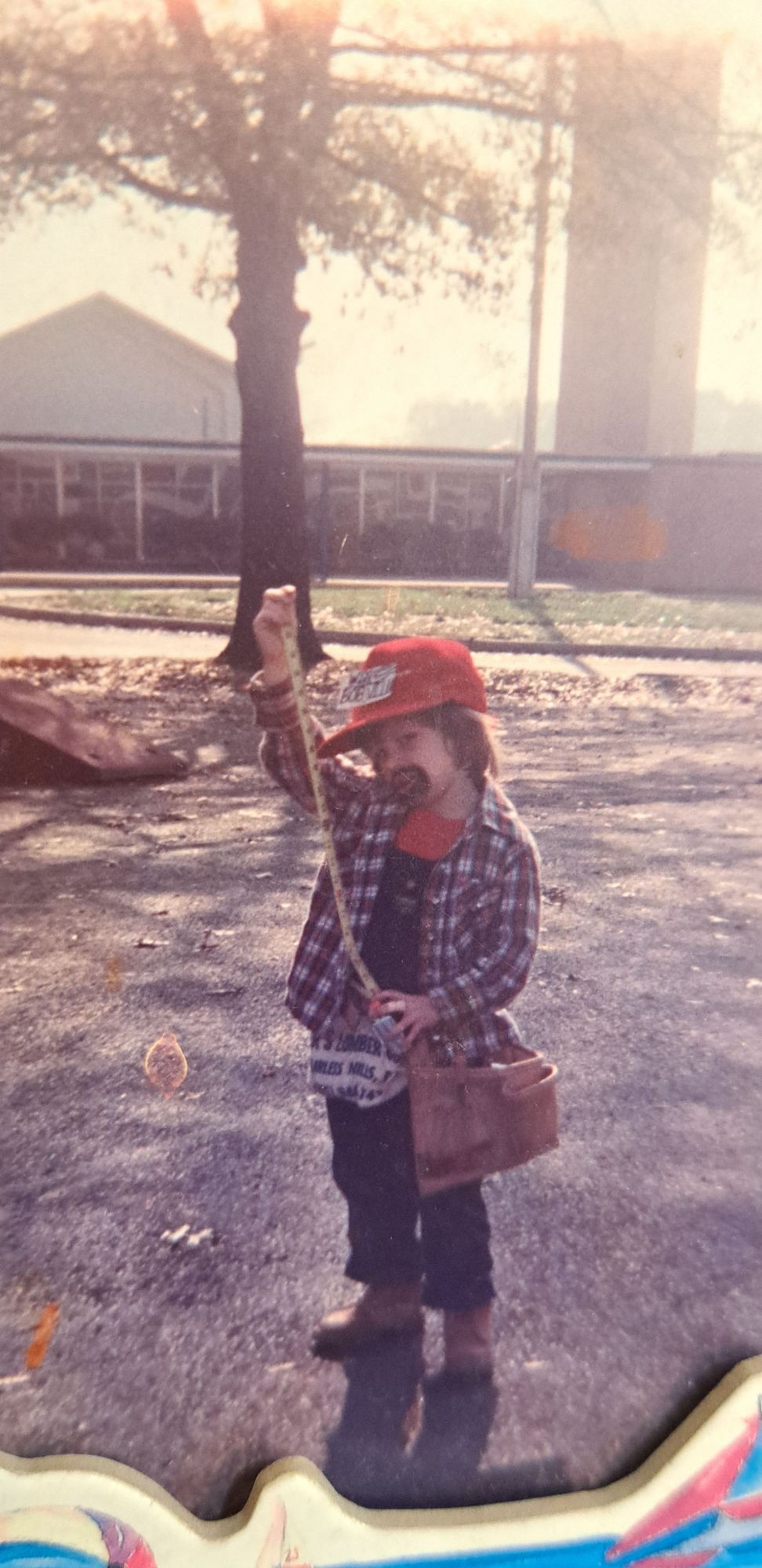 me at kindergarten age wearing a pair of overalls, a cap, a flannel, beat up work boots, a tool belt, and a nail bag.
im holding a tape measure and 20 minutes out about 2 feet or so, and i have a goatee drawn on.