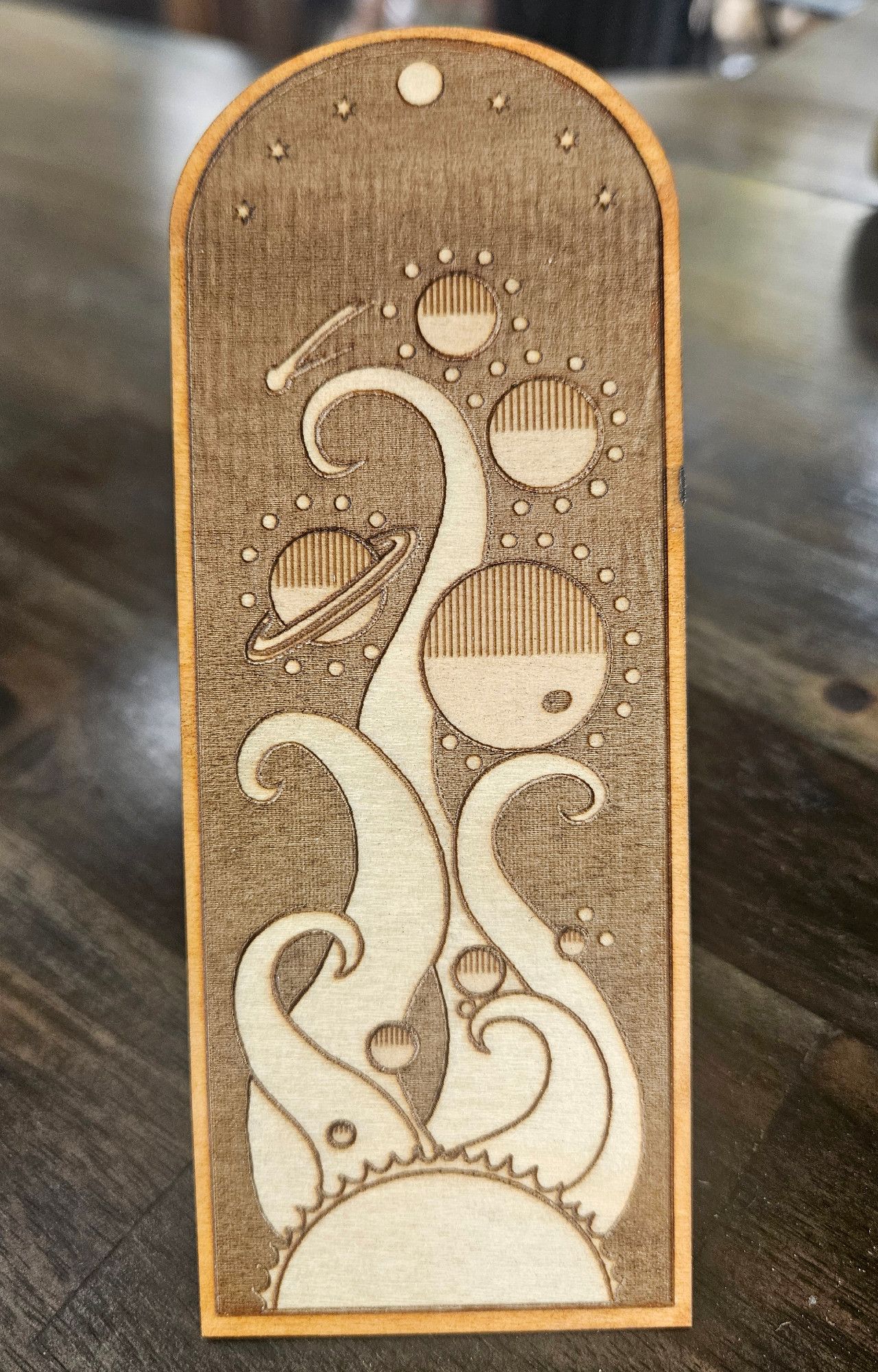 A wooden bookmark with a design of the planets of our solar system being cradled by rays from the sun