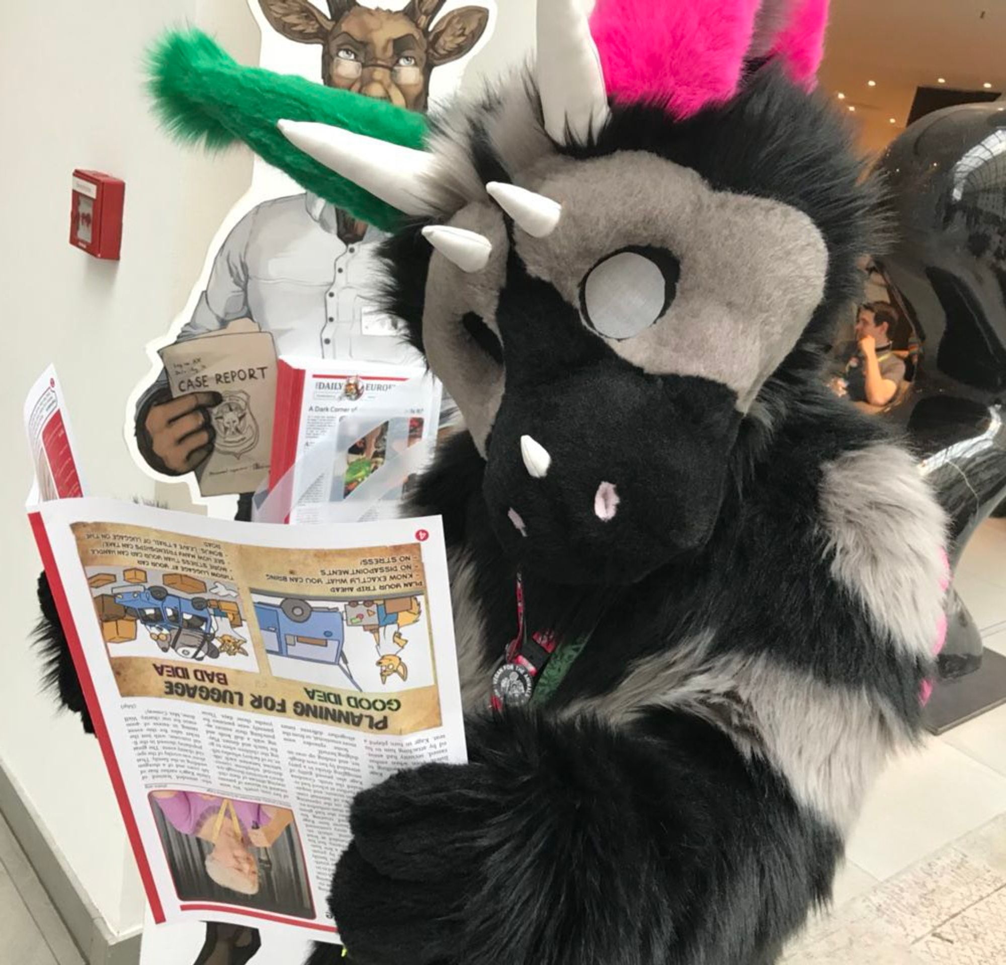 A Dutch Angel Dragon fursuiter holding a newspaper upside down in the lobby at a furry convention.