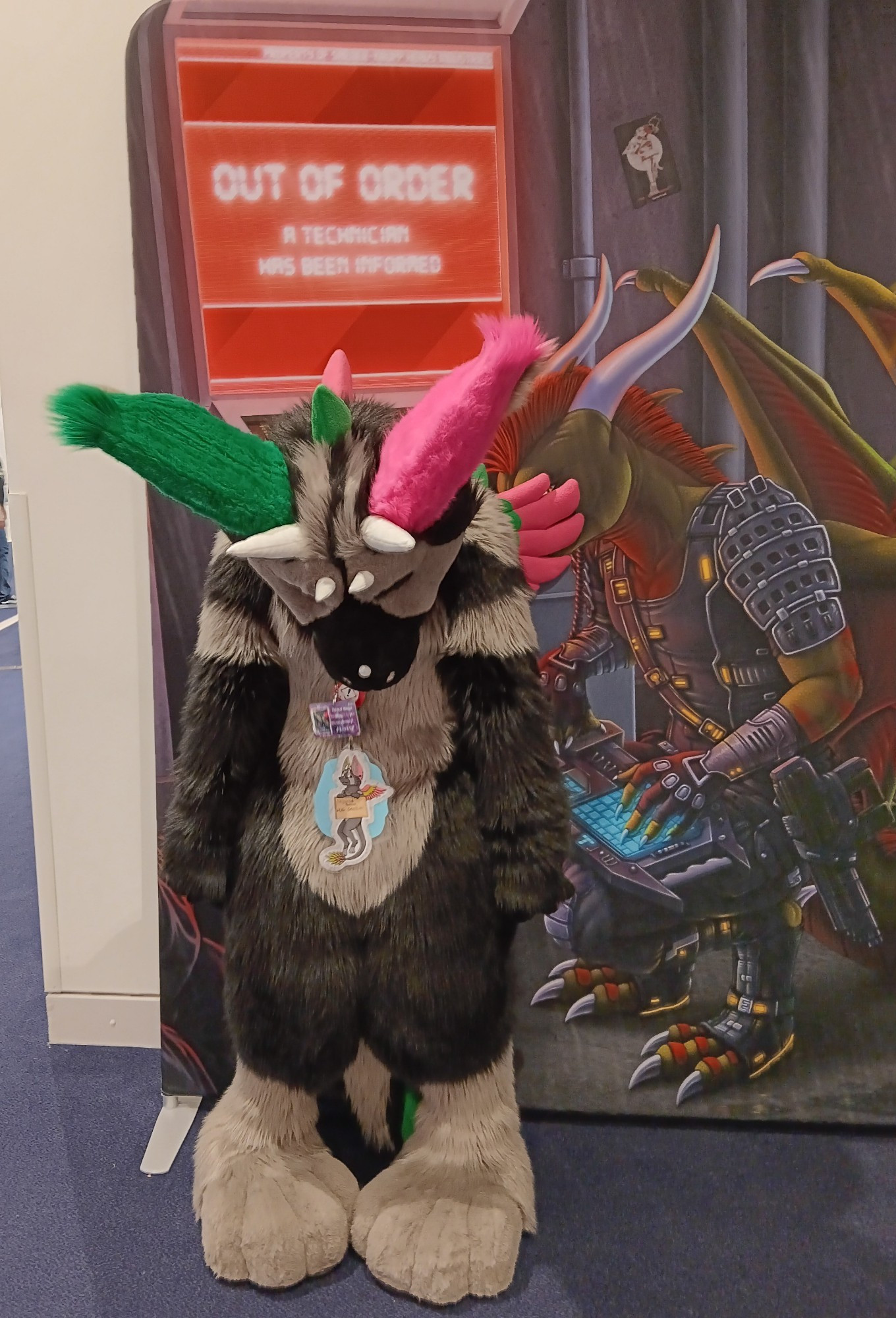 A Dutch angel dragon fursuiter standing with arms relaxed and head drooping down, in front of a sign that reads "out of order".