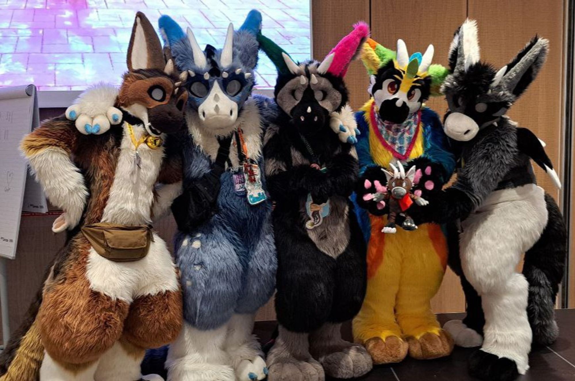 Photos of Dutch Angel Dragon fursuiters posing in a line, some with arms around each other.