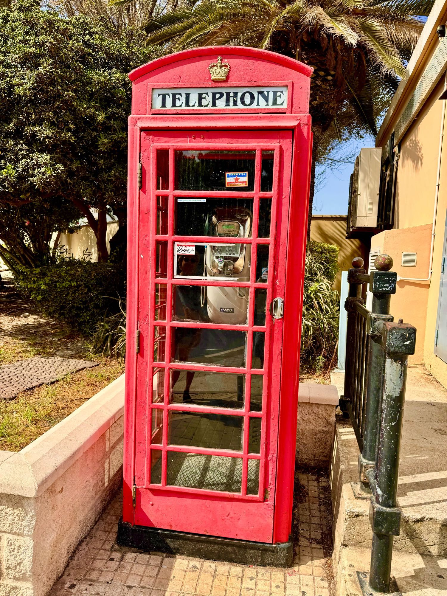 Eine rote Telefonzelle auf der ‚Telephone‘ geschrieben steht. Darüber eine goldene Krone.