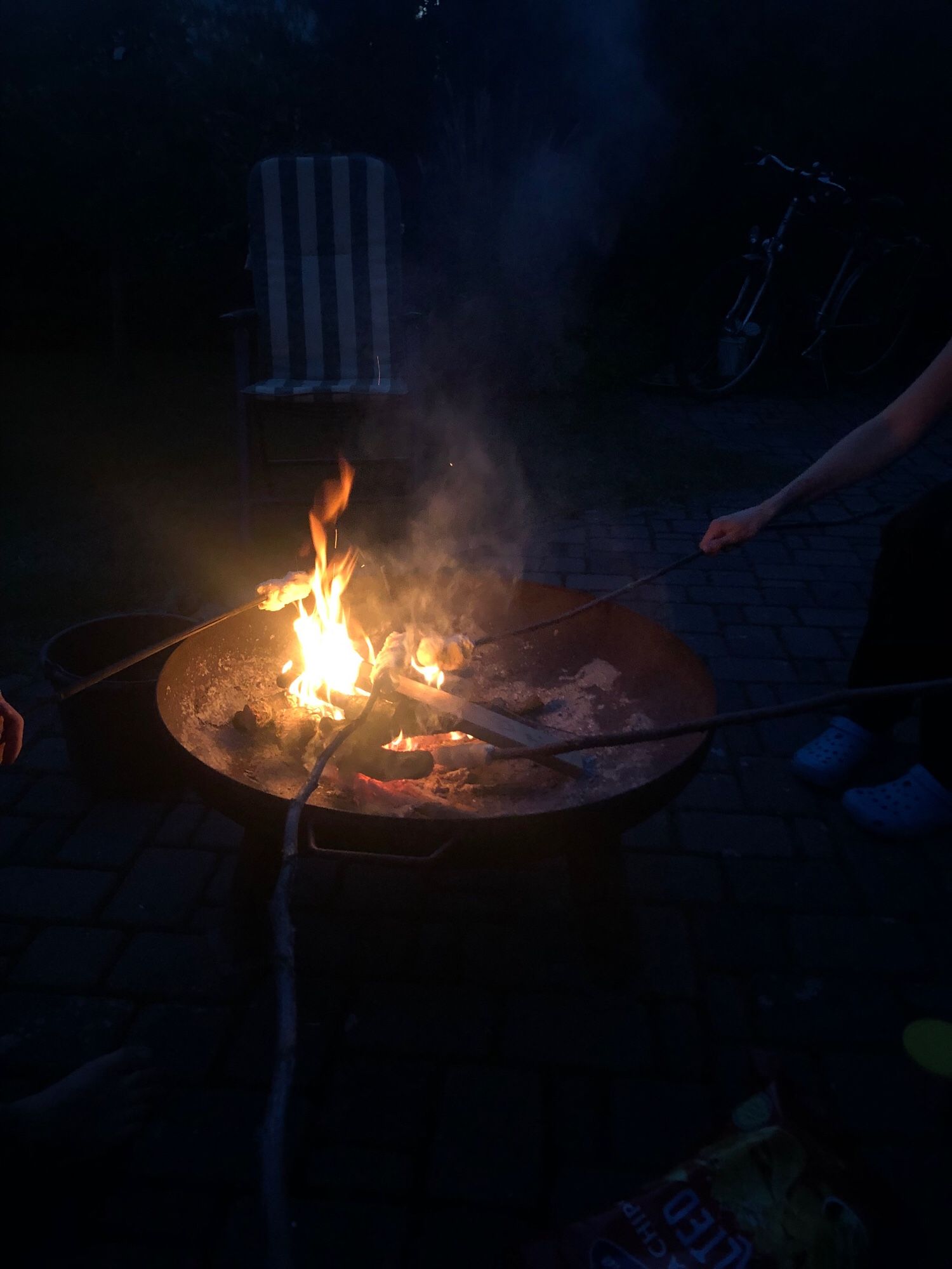 Im Dunkeln steht eine Feuerschale, über der Stockbrot gebacken wird.