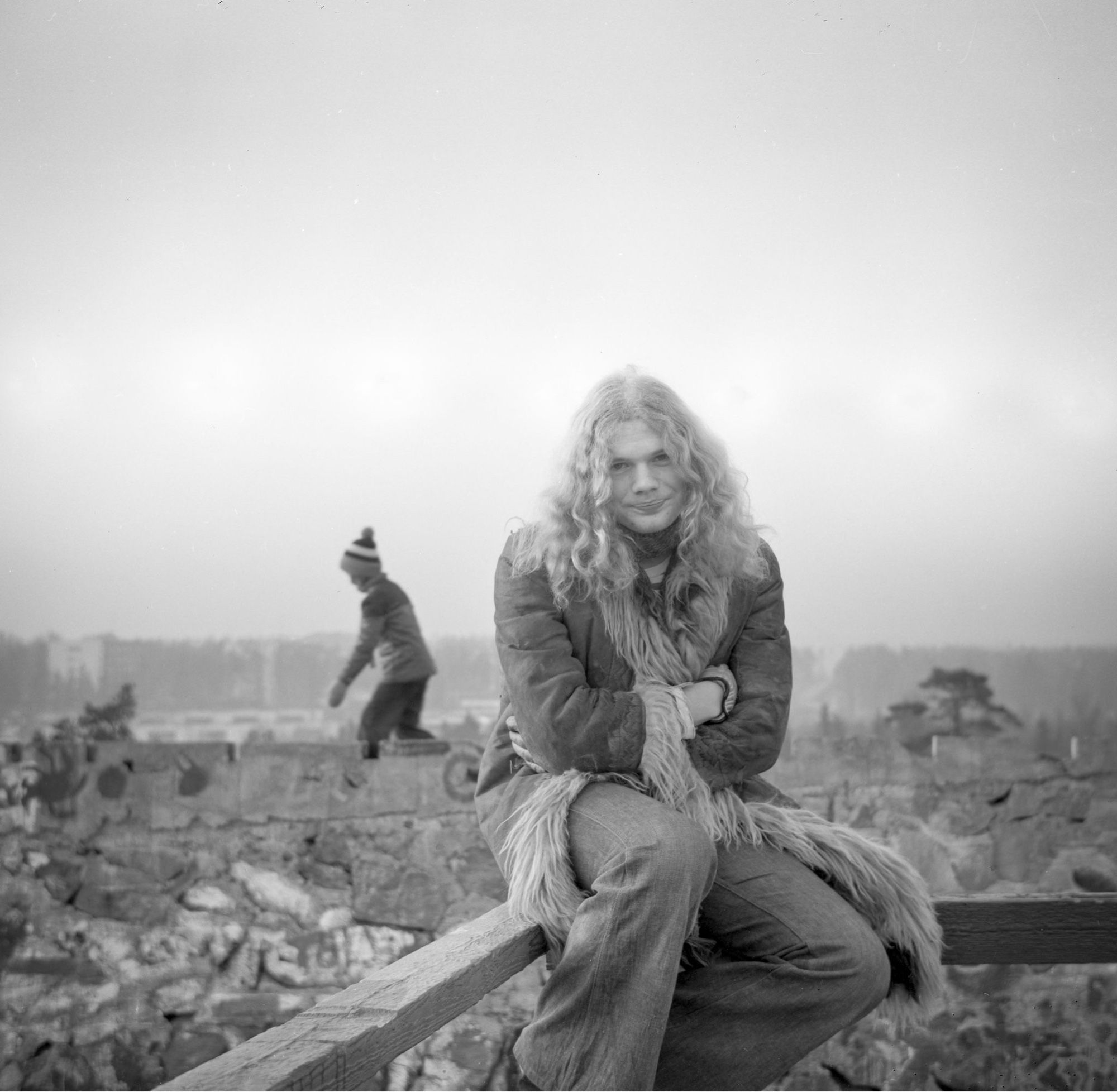 Man with long hair sitting on a fence.