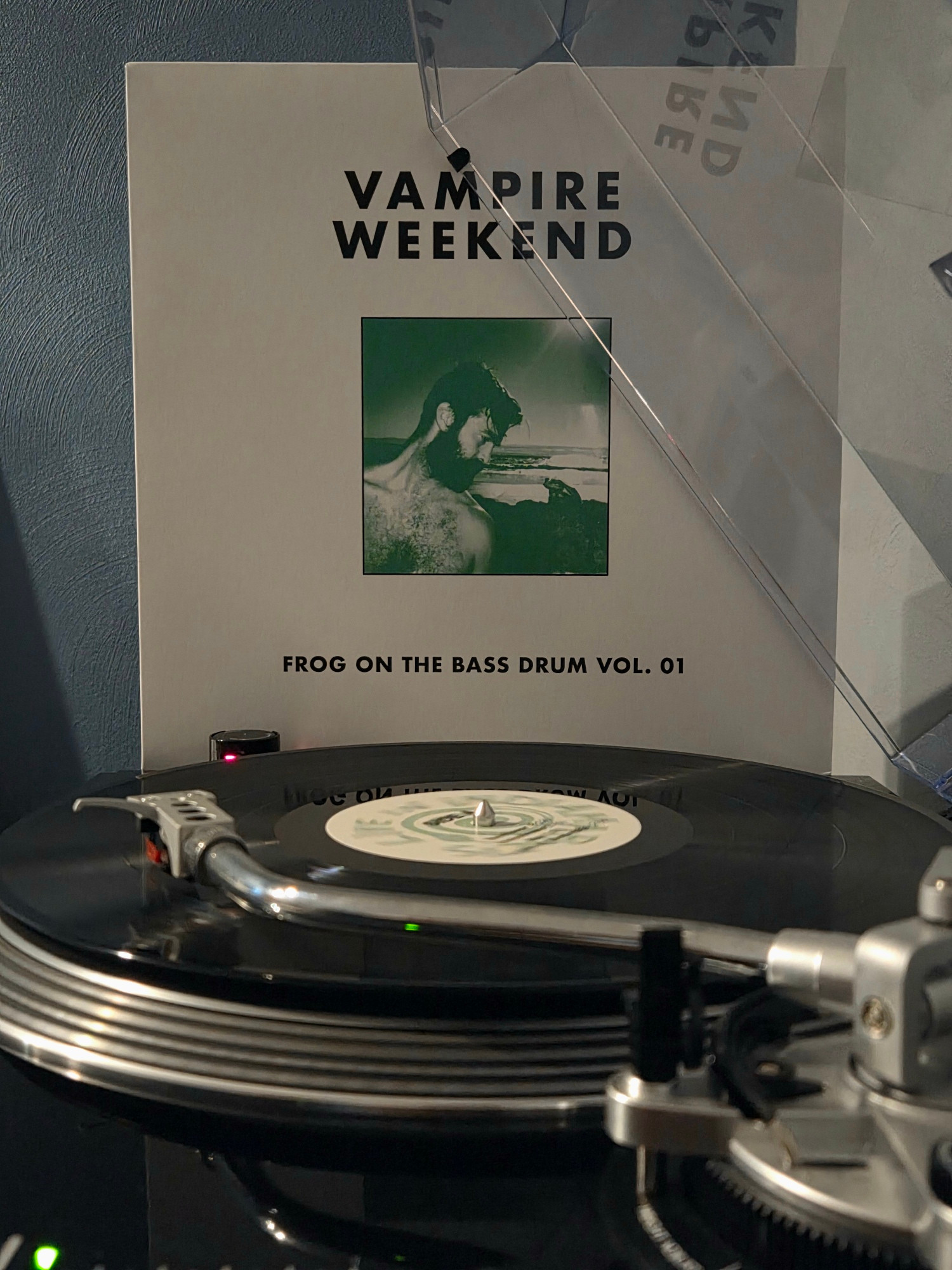 Side view of a black AT-LP120 spinning Frog on the Bass Drum Vol 1 by Vampire Weekend, its jacket propped up against the dust cover in the background