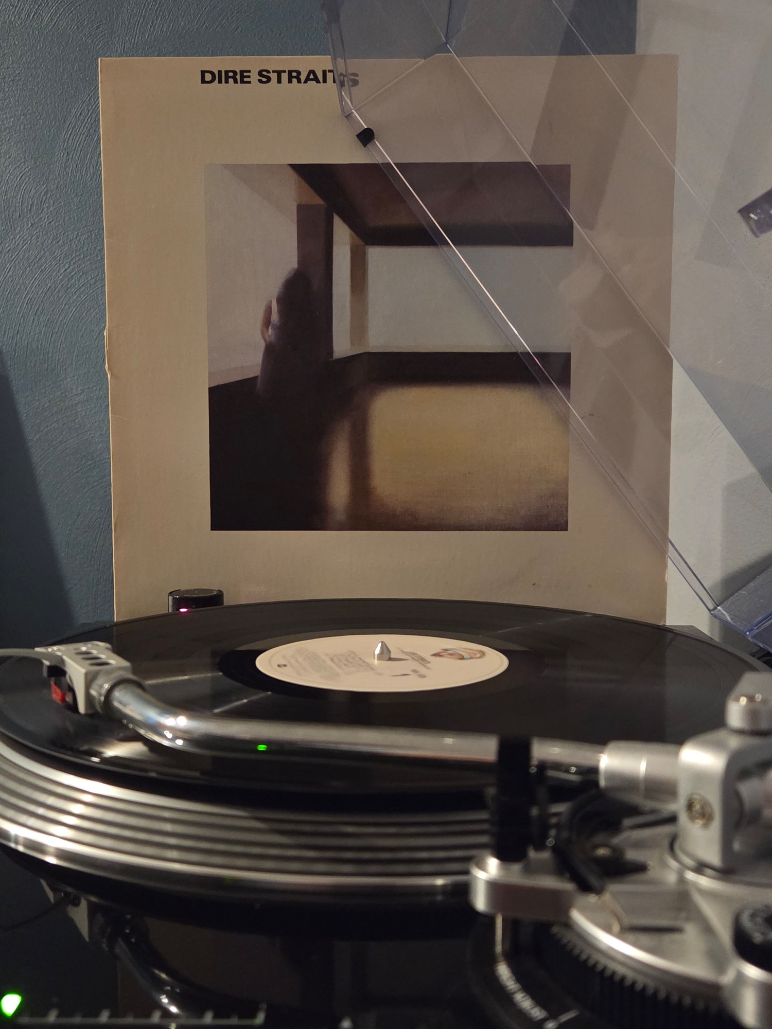 Side view of a black AT-LP120 spinning the self-titled debut album from Dire Straits, its jacket propped up against the dust cover in the background 