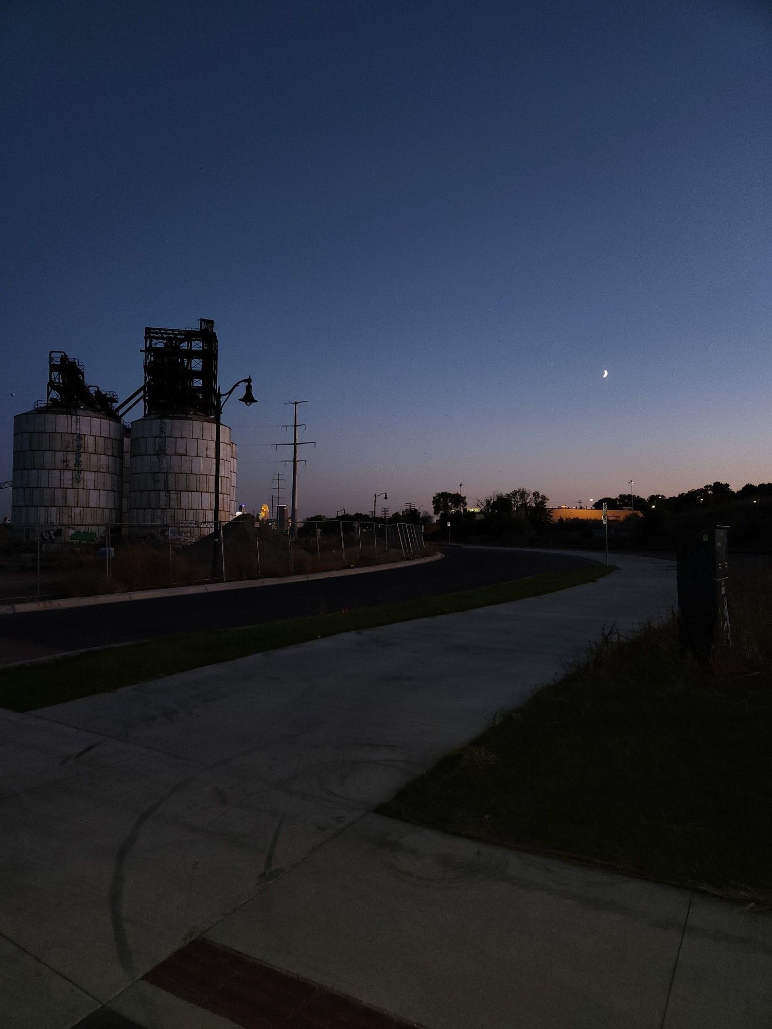 concrete bike trail, with 2 round building off to the left. Blue evening sky, with a slight orange glow.